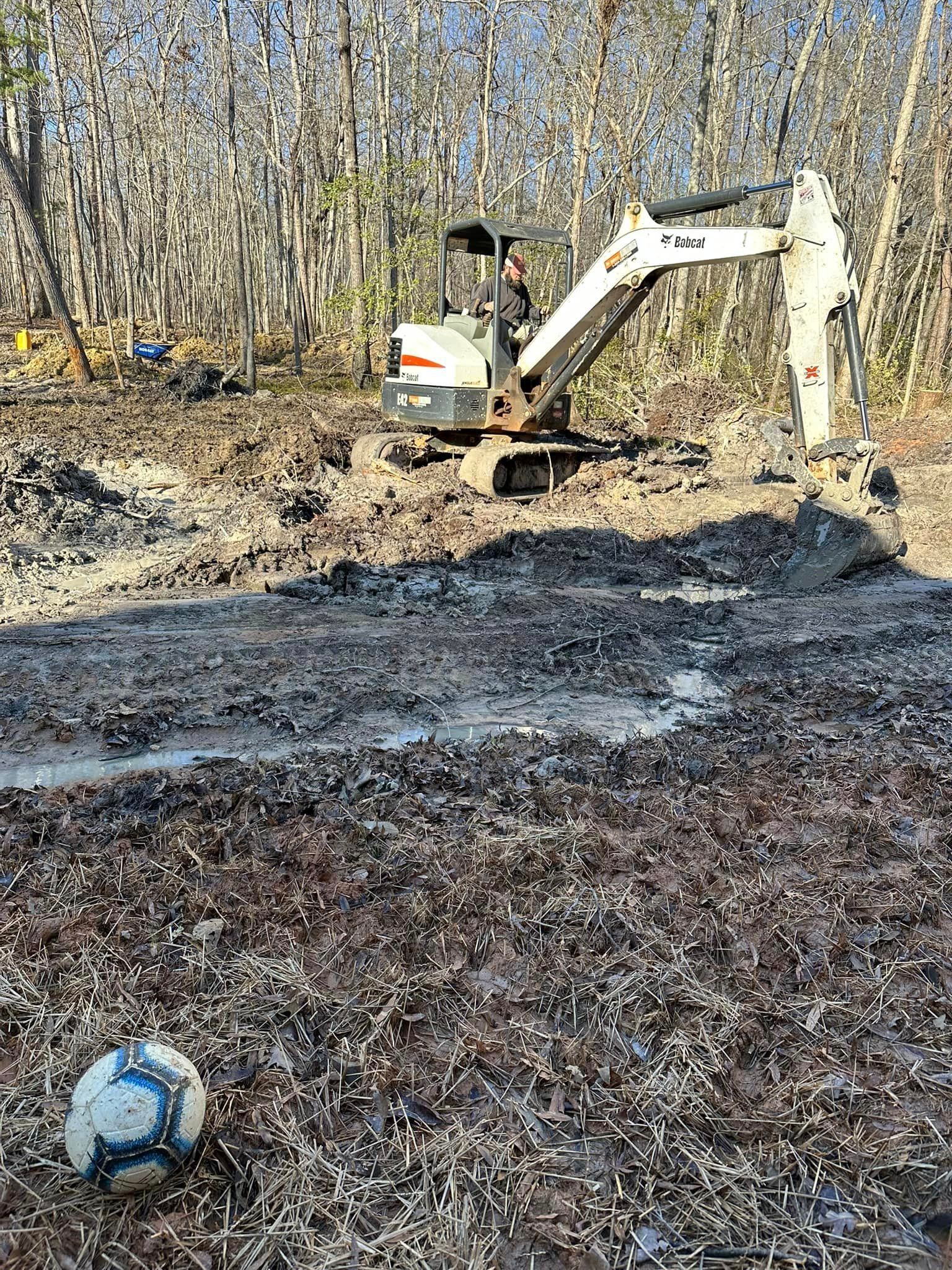 A soccer ball is sitting in the mud next to a bulldozer.