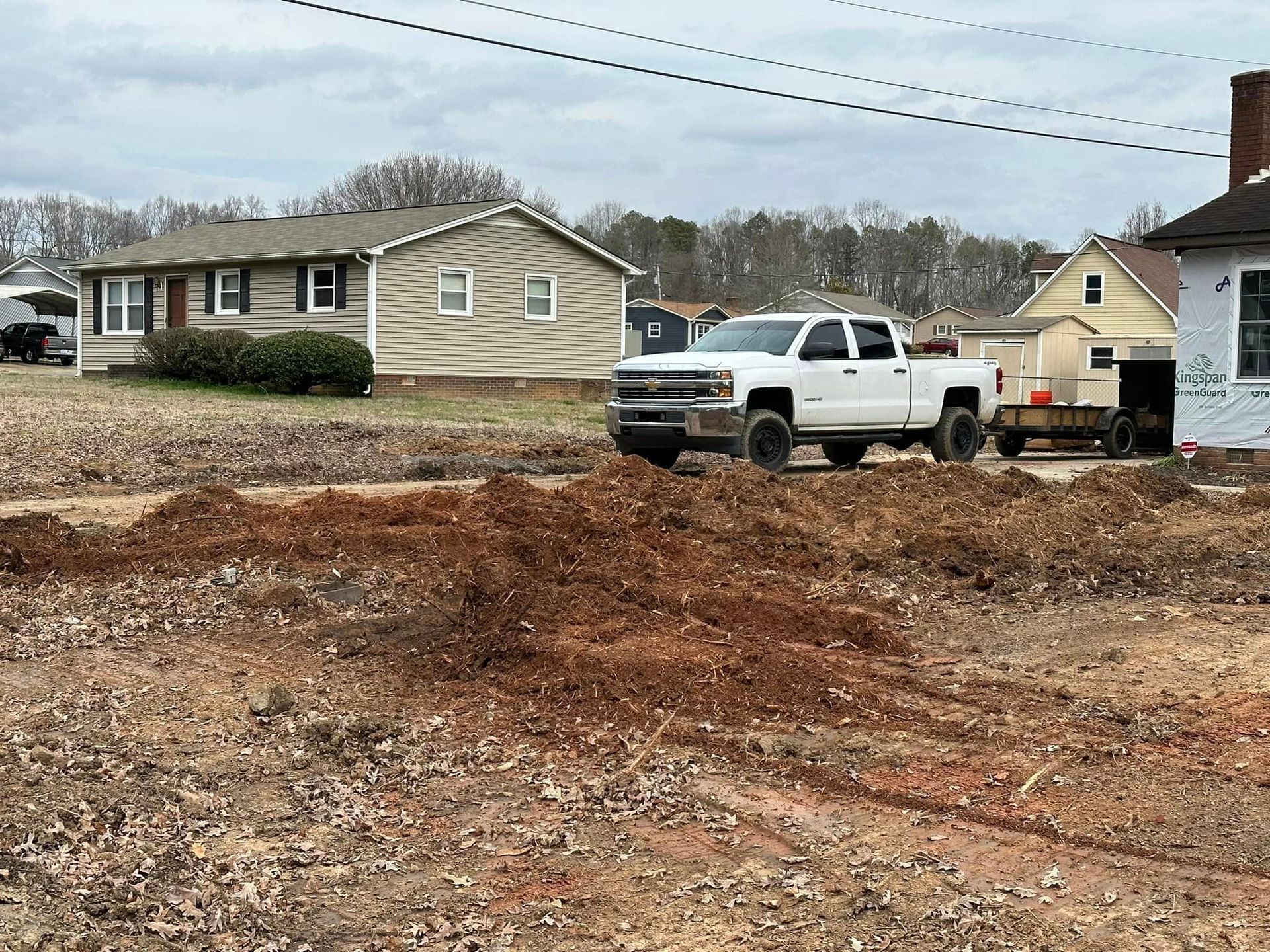 A white truck is parked in a dirt field in front of a house.