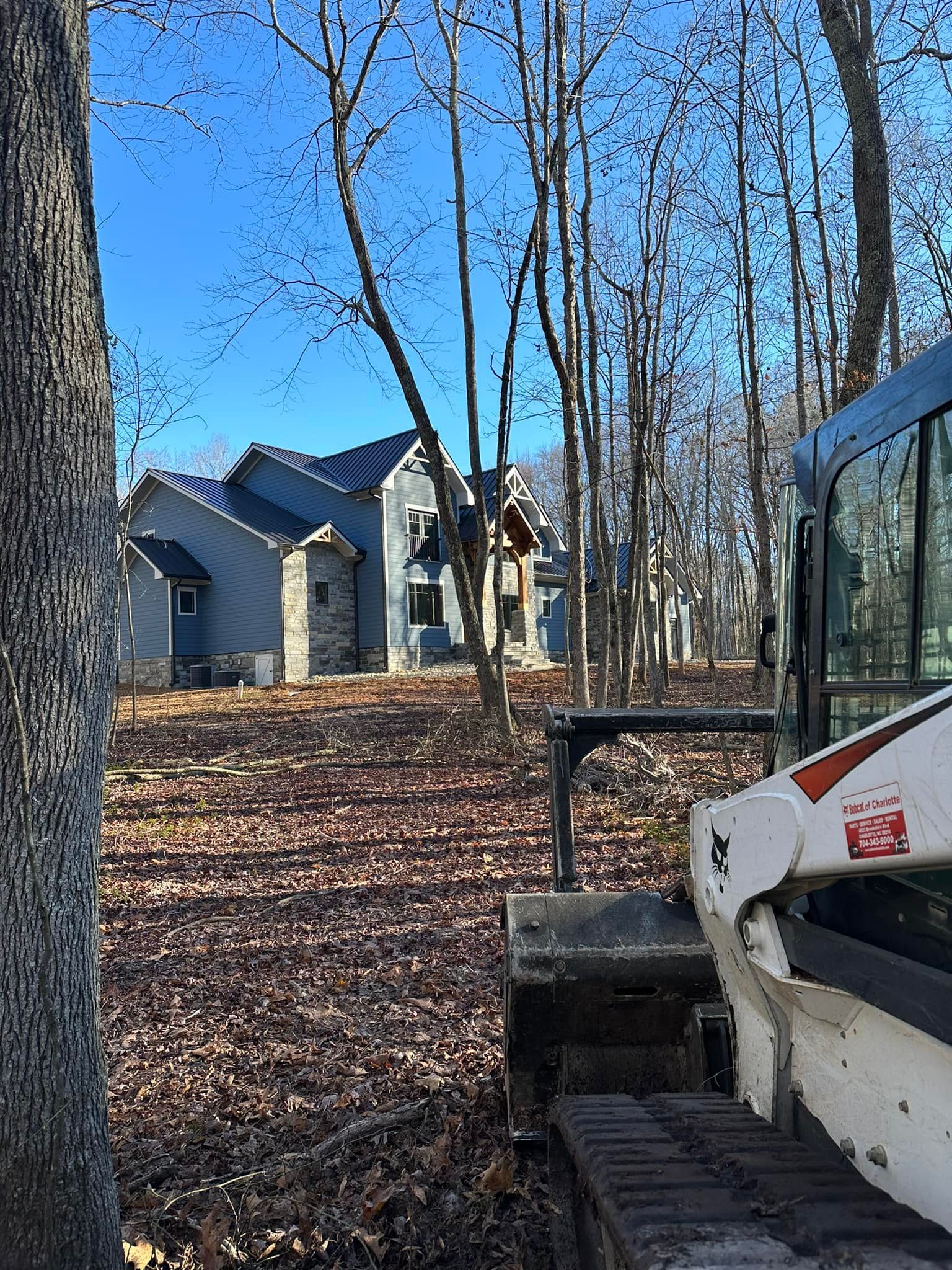 A bulldozer is parked in front of a house in the woods.