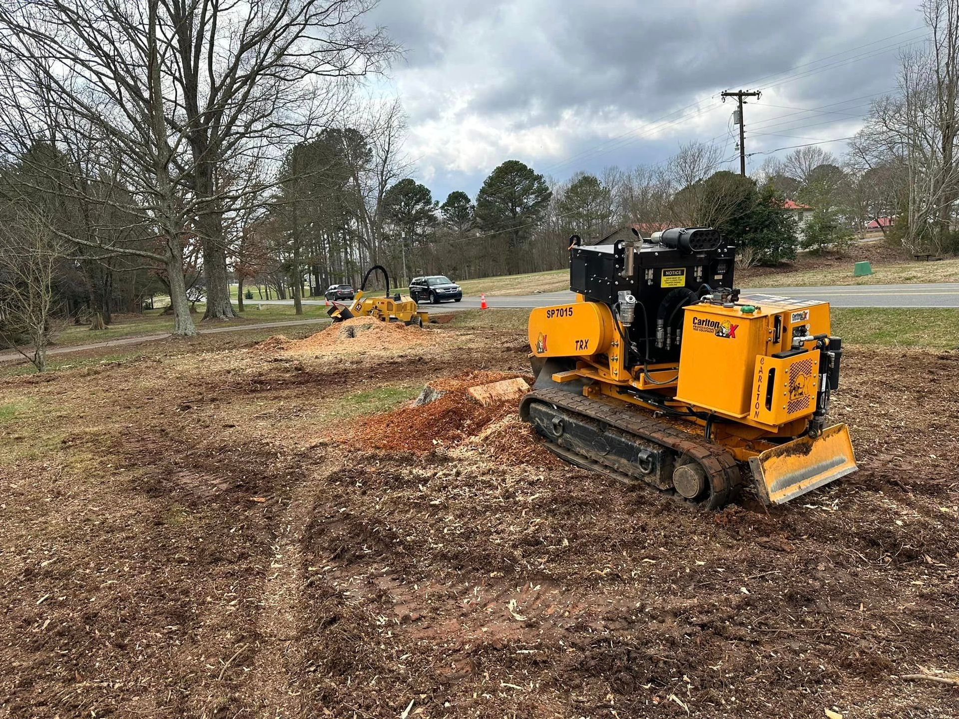 A yellow tractor is cutting a tree stump in a field.
