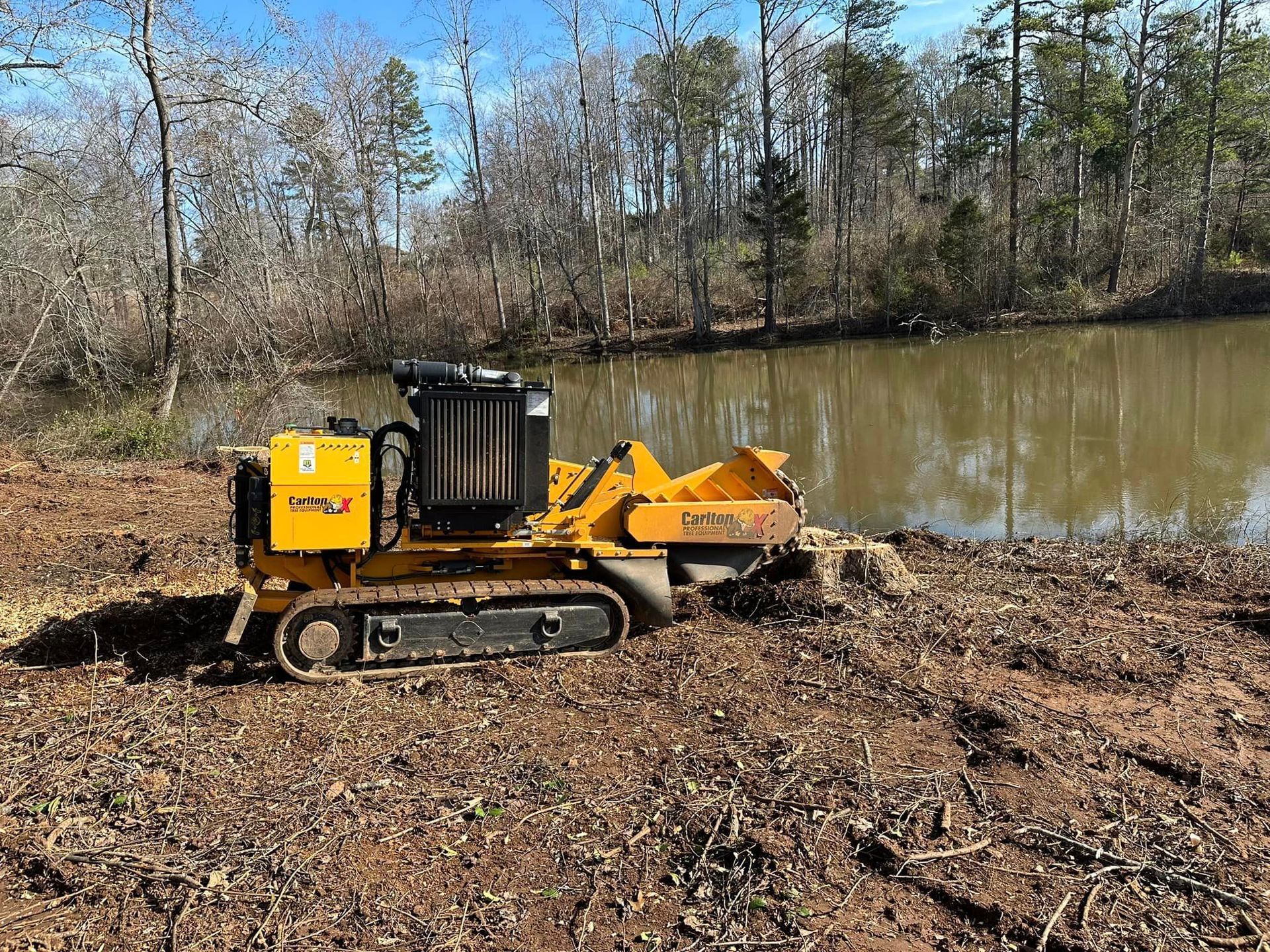 A yellow stump grinder is sitting next to a body of water.