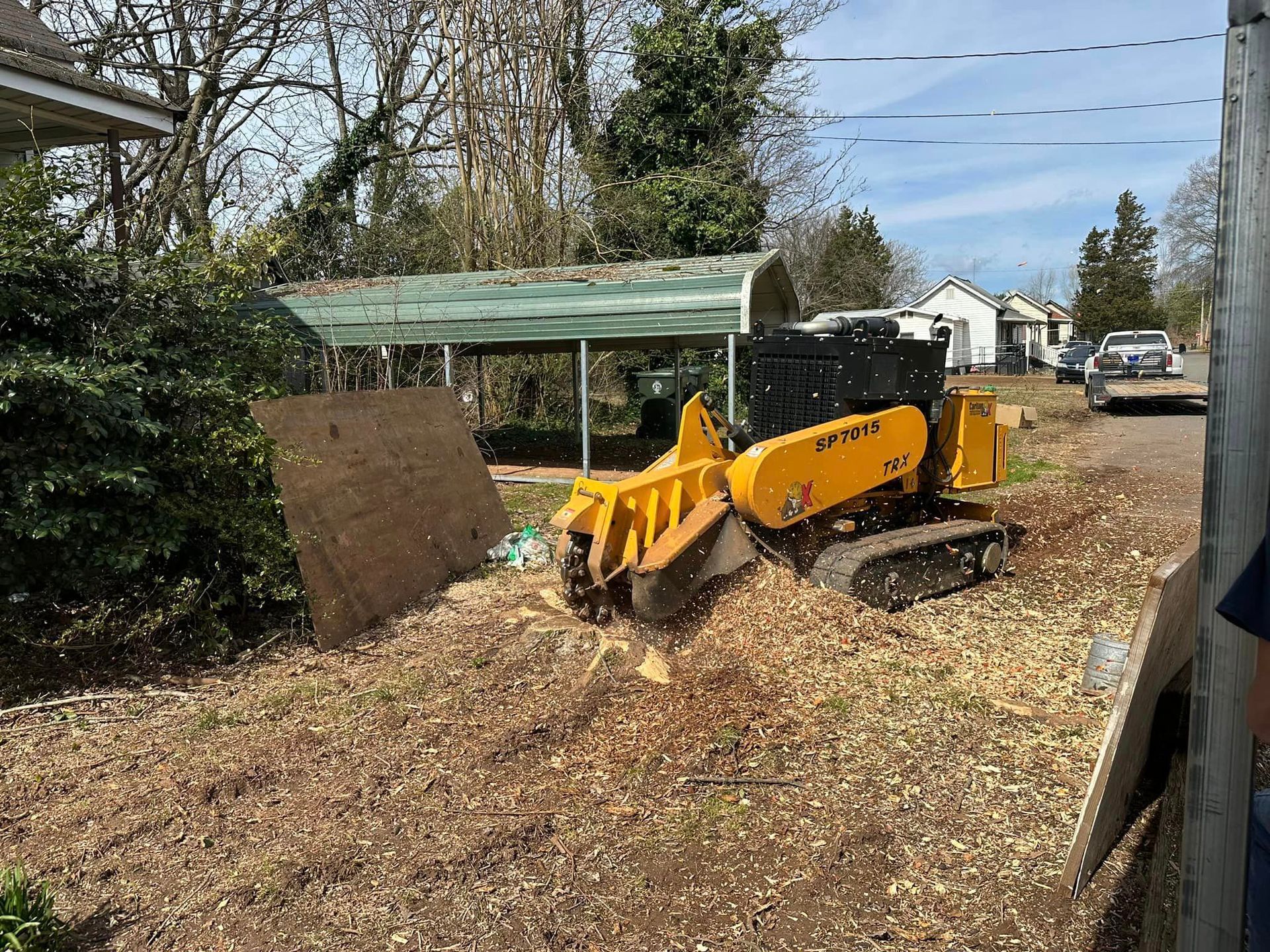 A yellow tractor is cutting a tree stump in a yard.