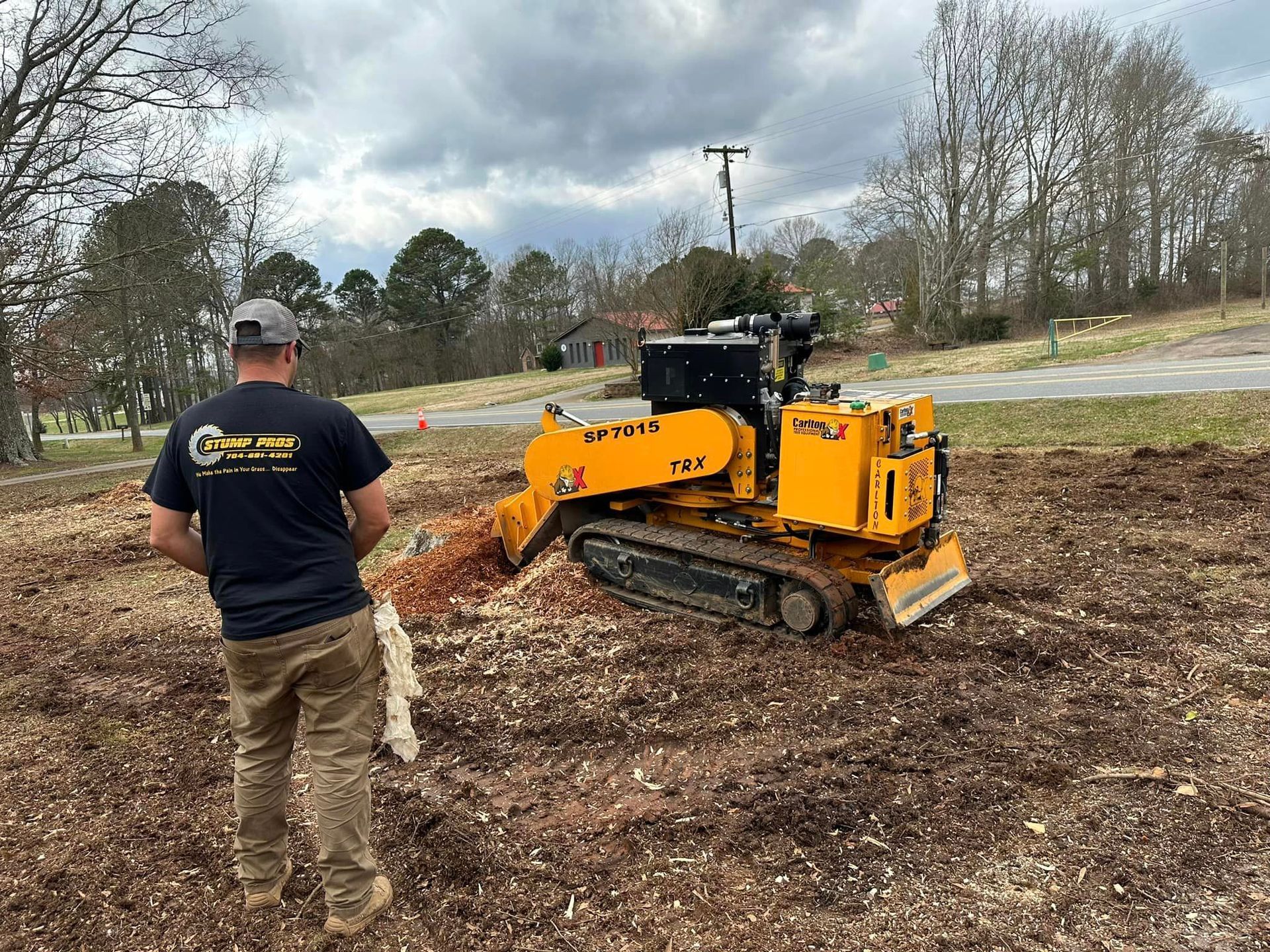 A man is standing in front of a stump grinder in a field.