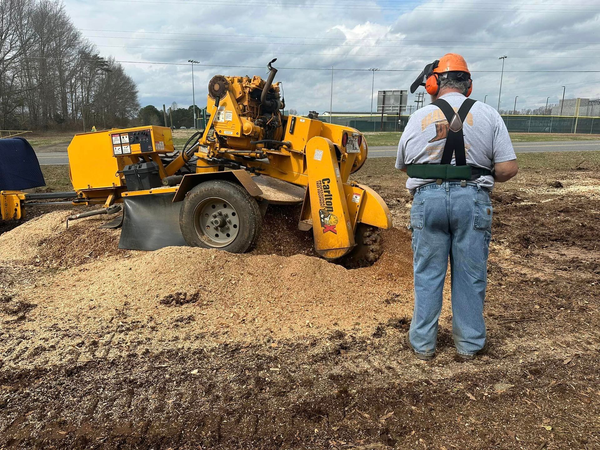 A man is standing in front of a stump grinder in a field.