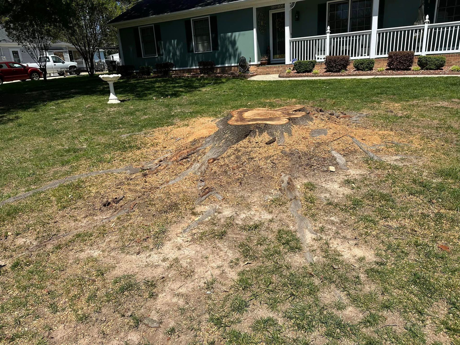 A tree stump in the grass in front of a house.