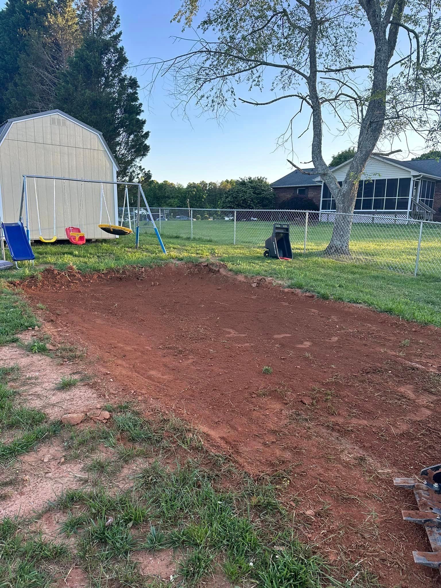 A dirt road going through a grassy field with a house in the background.
