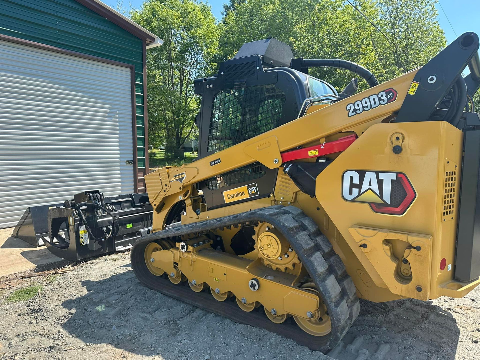A yellow cat skid steer is parked in front of a garage.