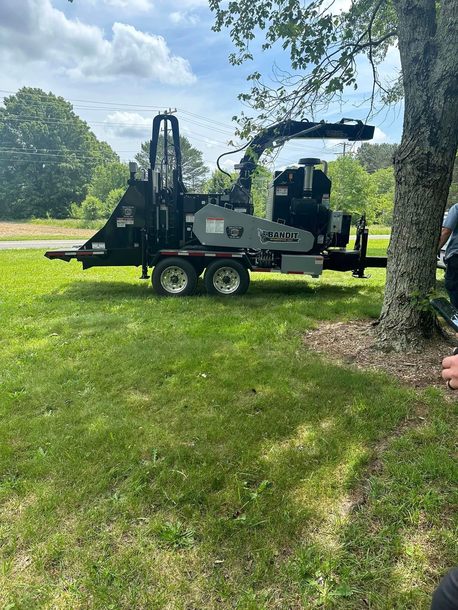 A tree chipper is parked in a grassy field next to a tree.