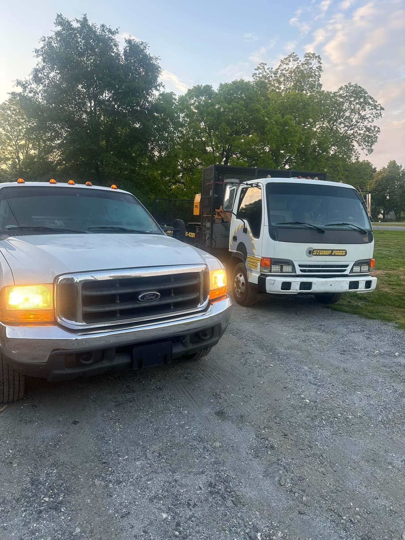 Two white trucks are parked next to each other on a gravel road.