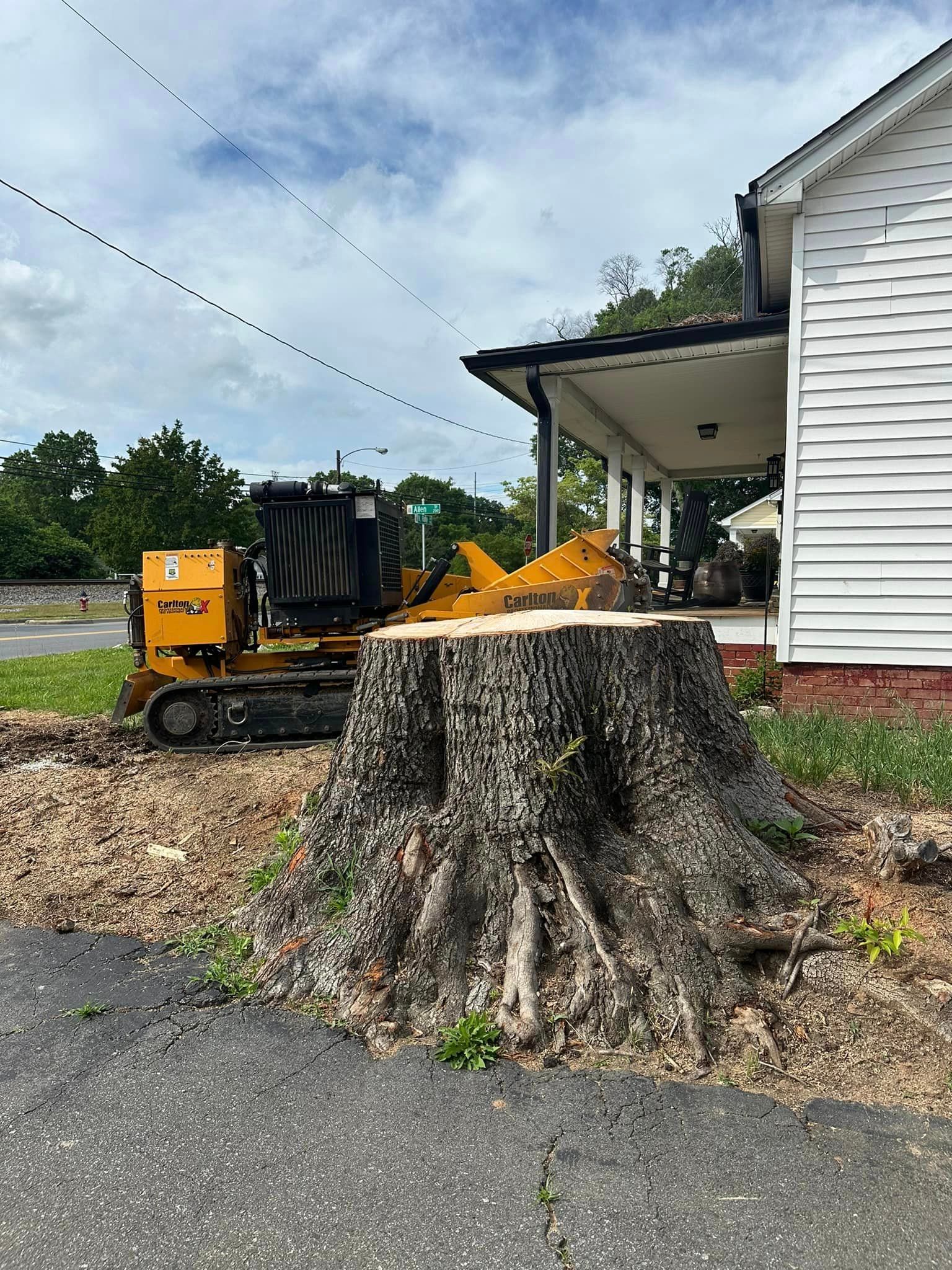 A large tree stump is being removed by a machine in front of a house.