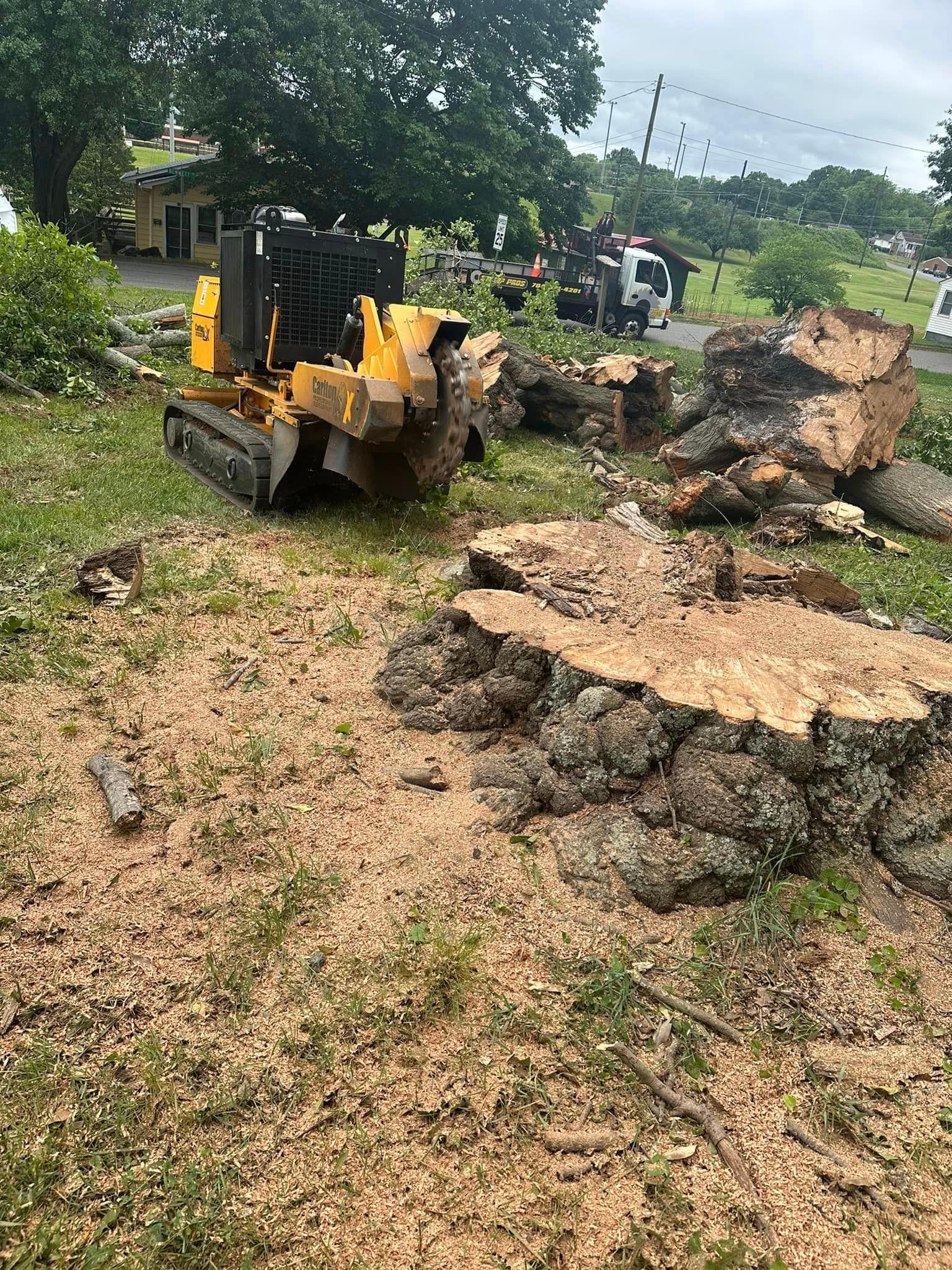 A tractor is cutting down a tree stump in a yard.