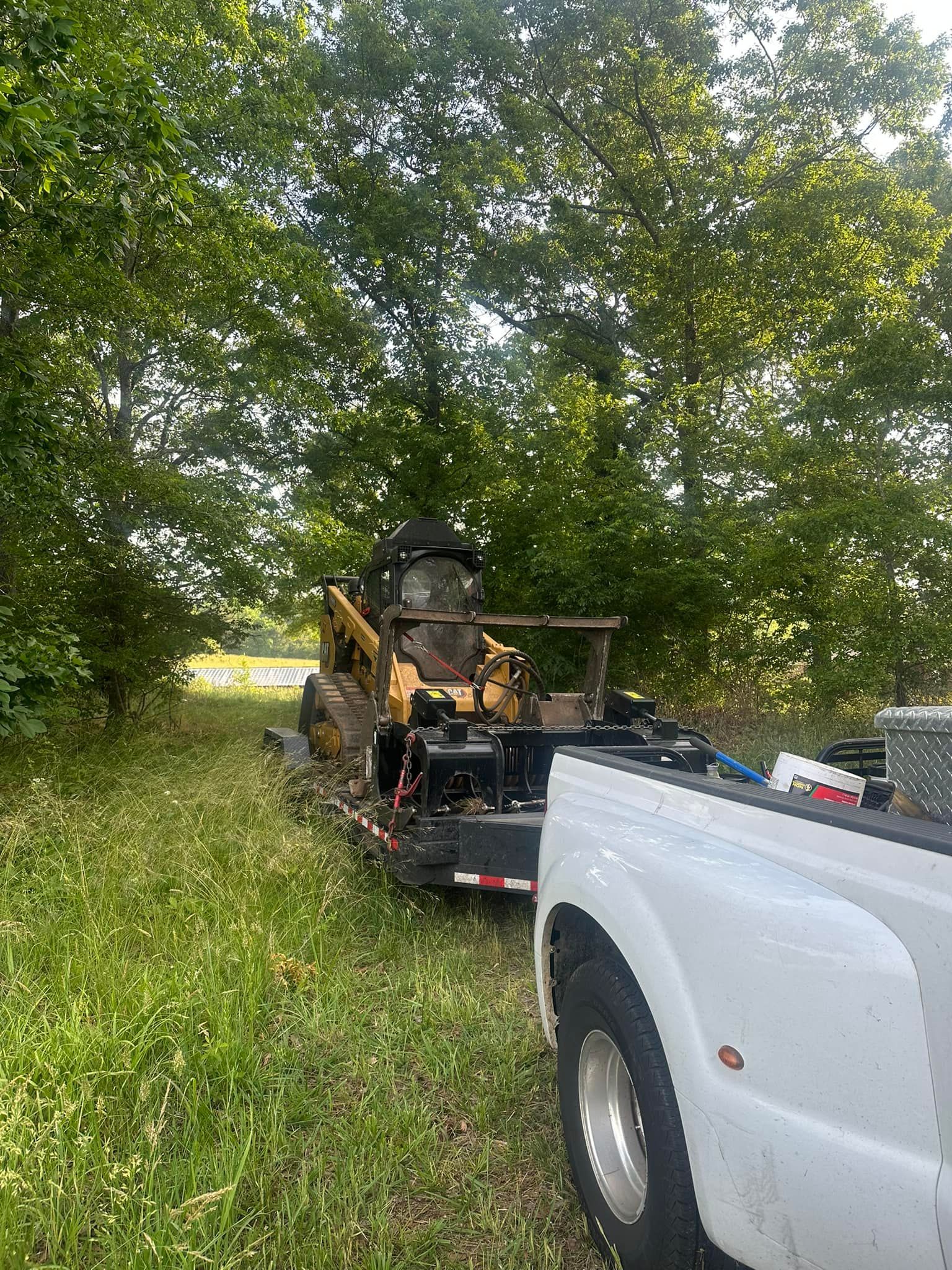 A bulldozer is parked in the grass next to a white truck.