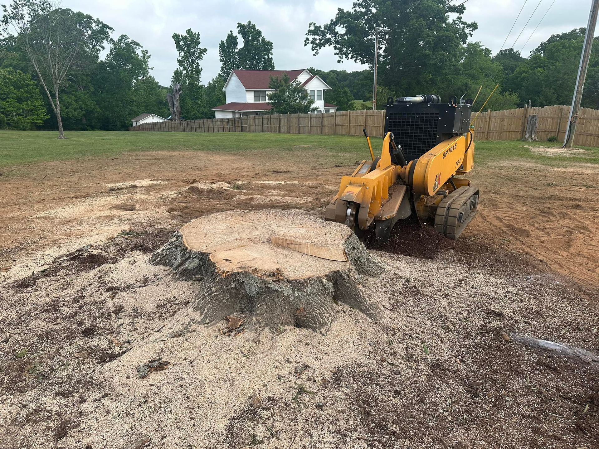 A yellow tractor is cutting a tree stump in a field.