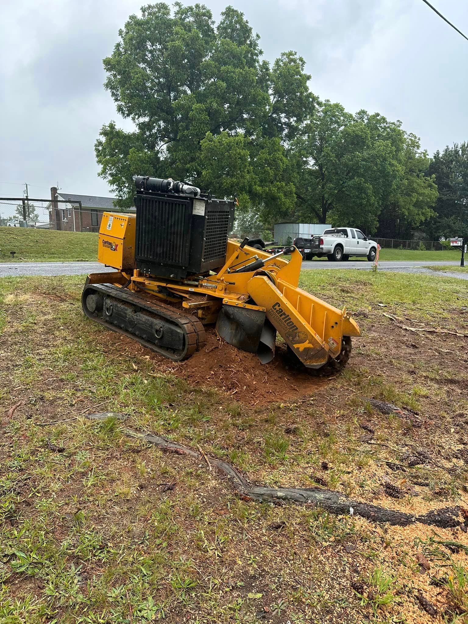A yellow stump grinder is sitting in the middle of a grassy field.