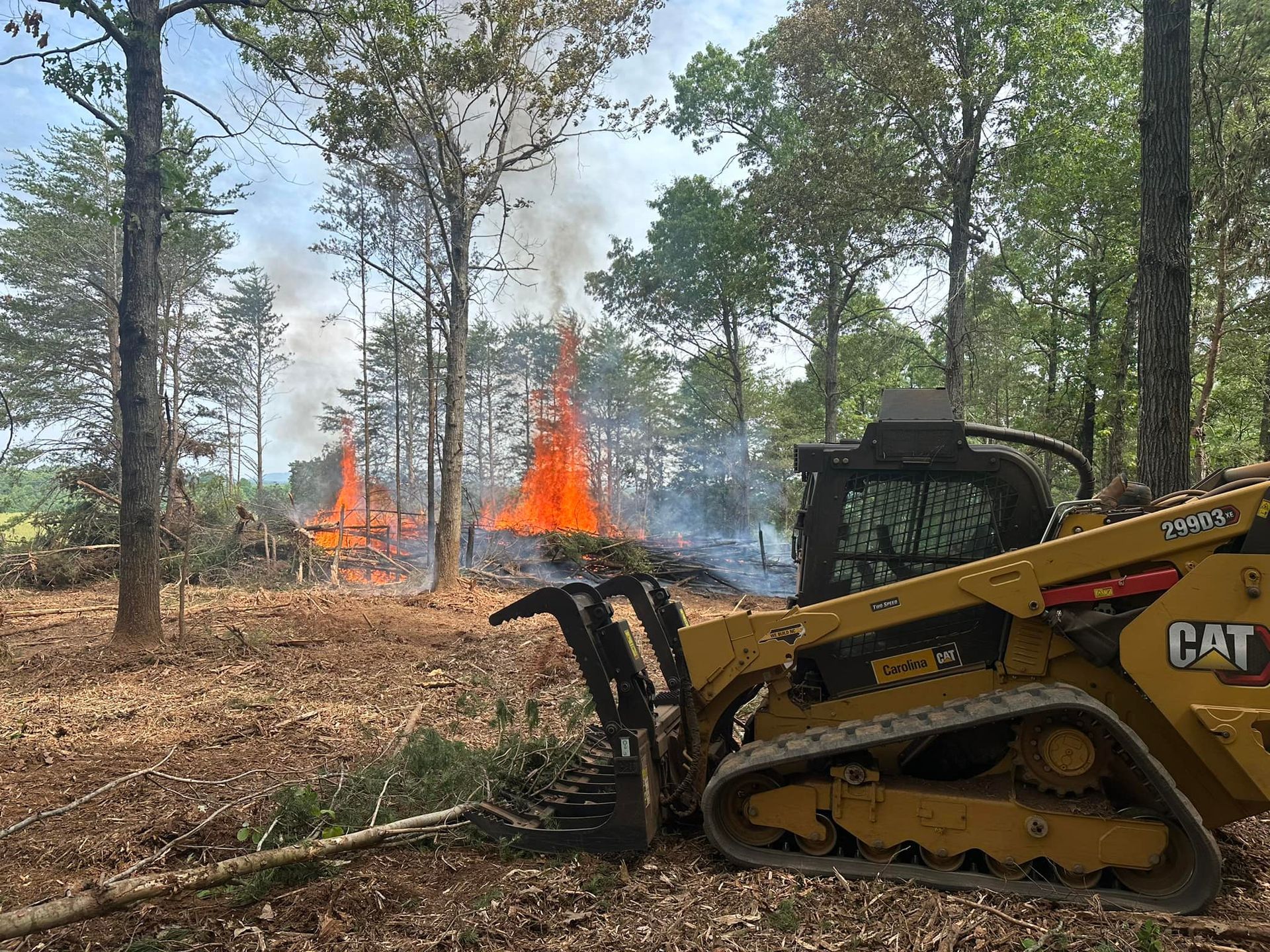 A bulldozer is sitting in the middle of a forest with a fire in the background.