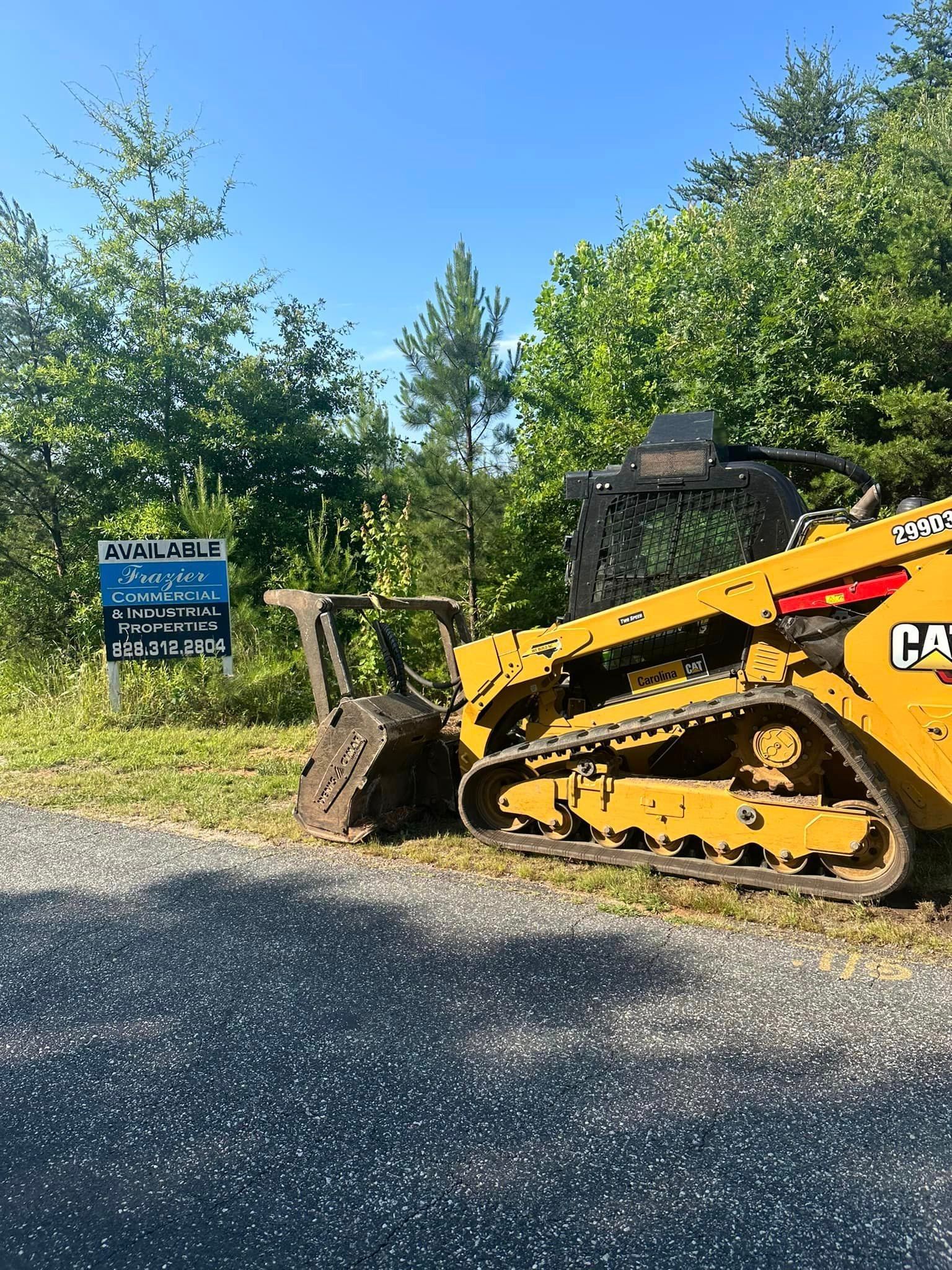 A bulldozer is parked on the side of the road next to a for sale sign.
