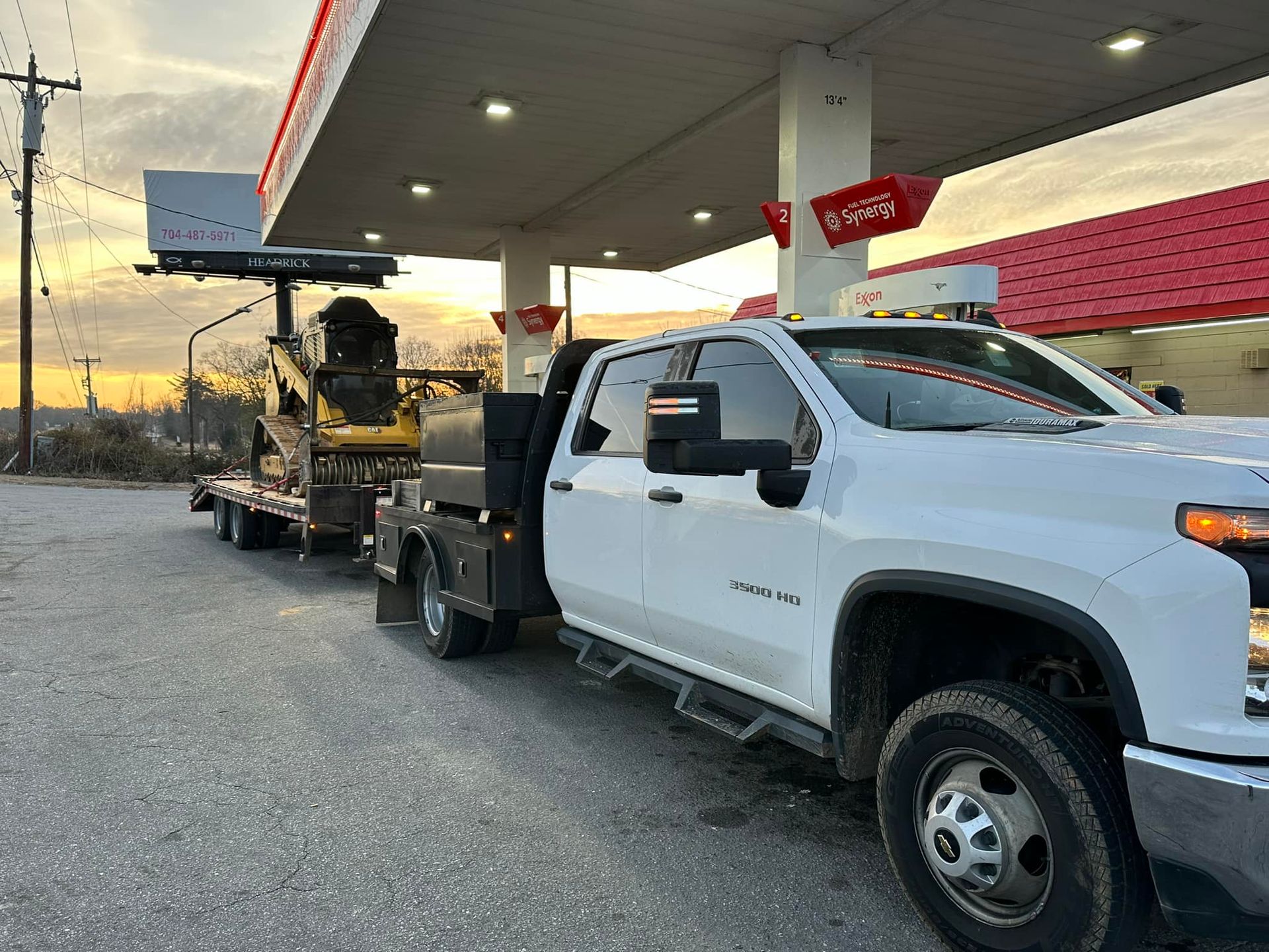 A white truck with a trailer attached to it is parked in front of a gas station.