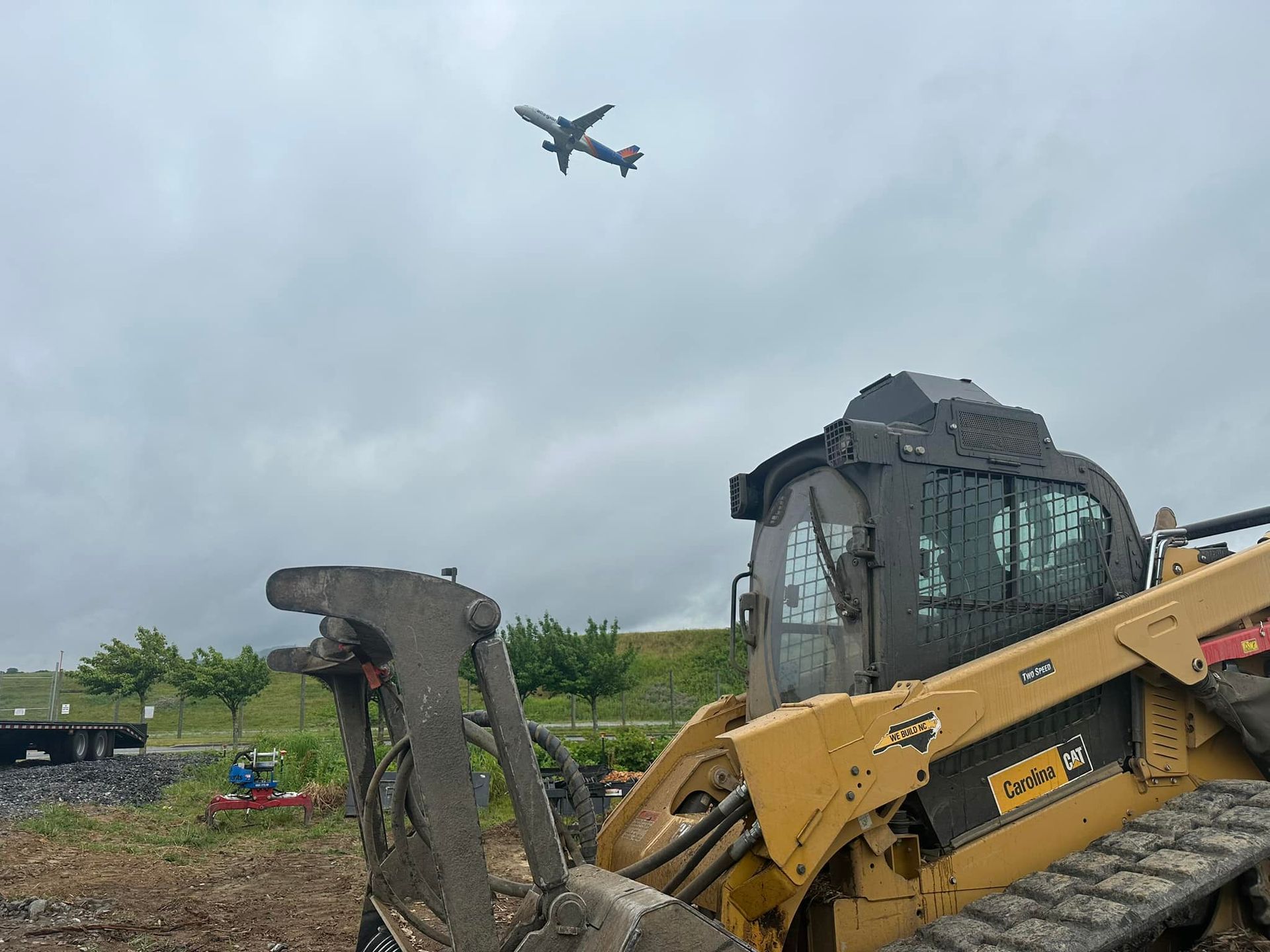 A plane is flying over a construction site with a bulldozer in the foreground.
