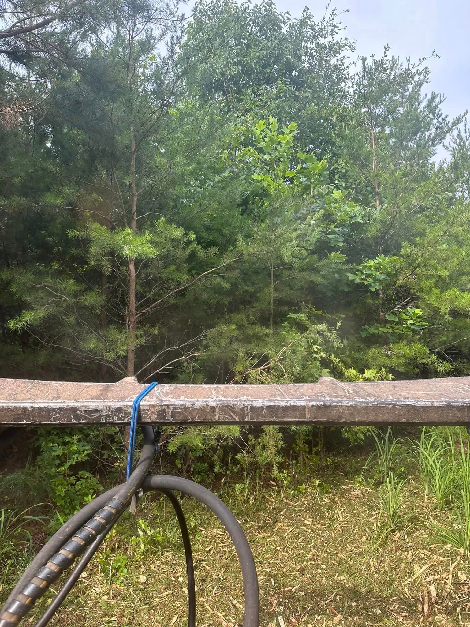 A hose is attached to a railing in a field with trees in the background.