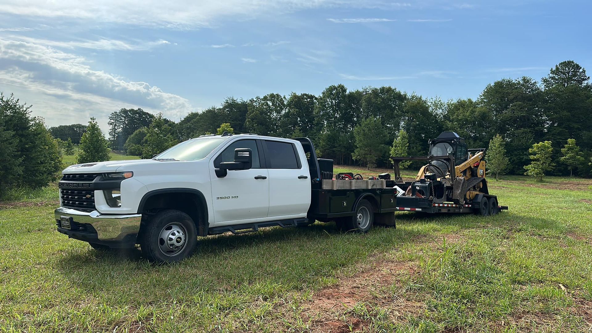 A white truck is towing a lawn mower in a field.