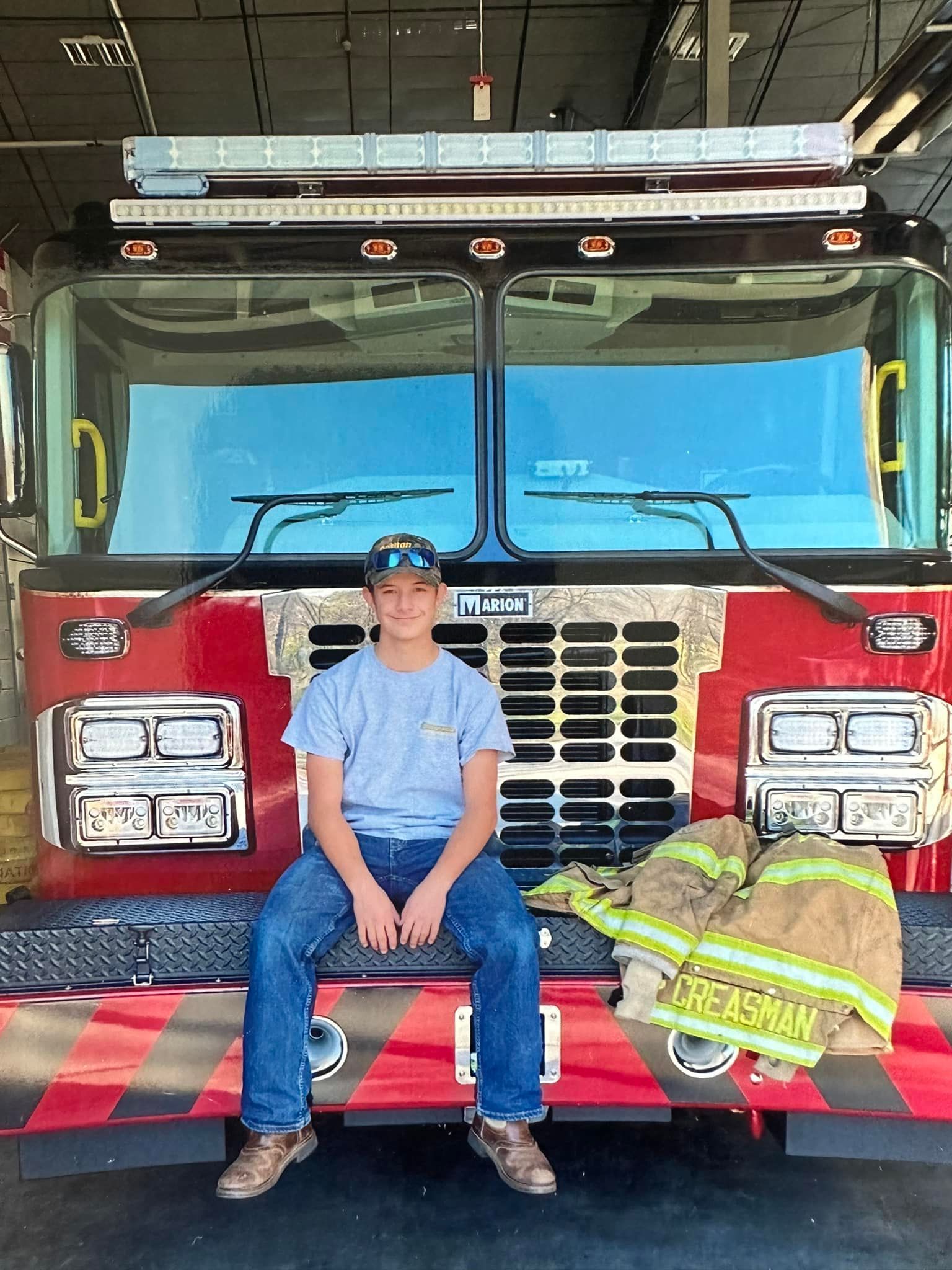 A young boy is sitting on the front of a fire truck.