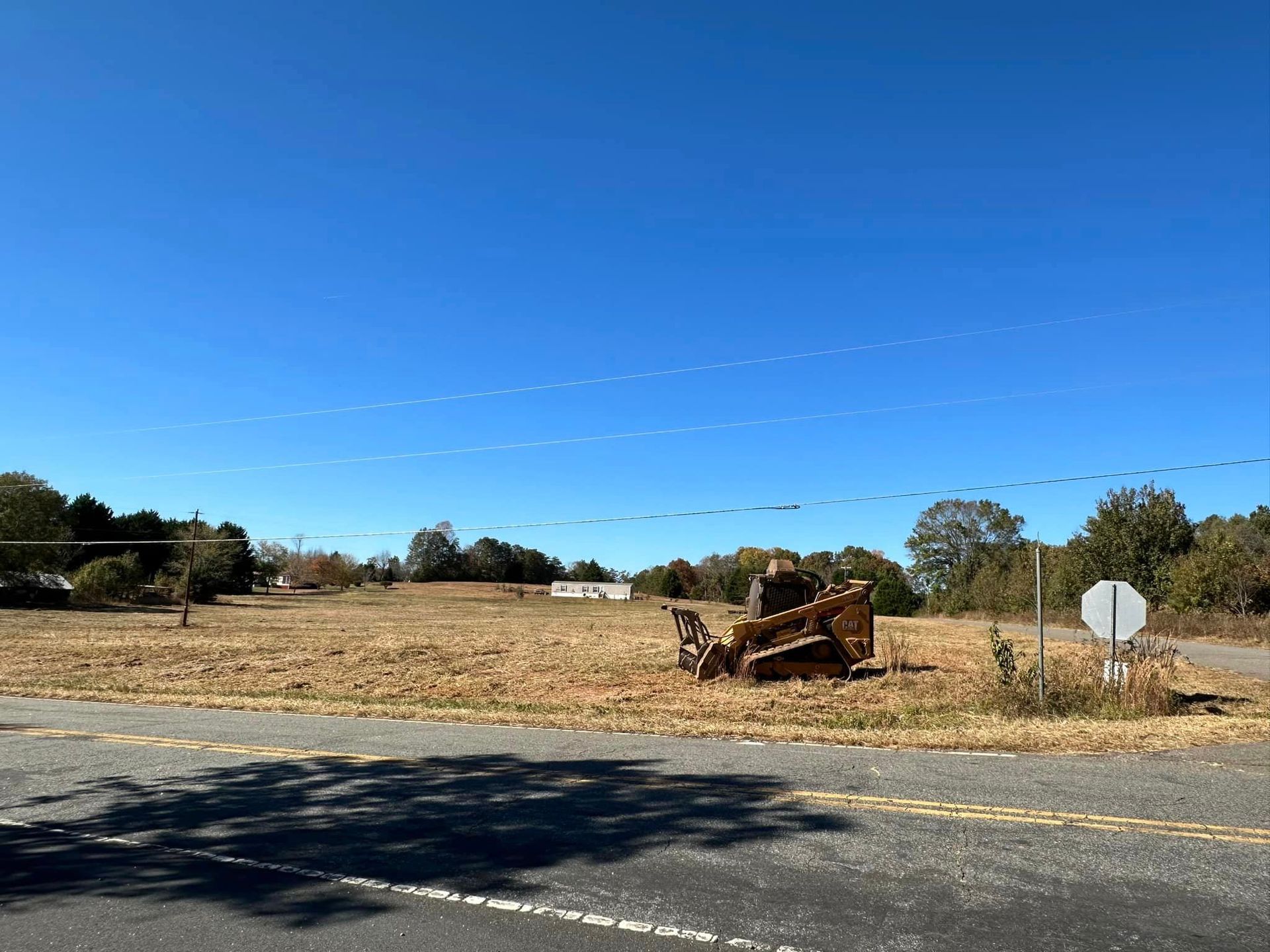 A bulldozer is sitting in the middle of a field next to a road.