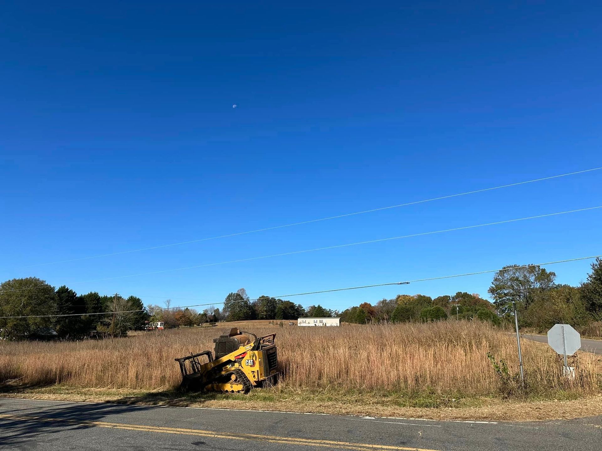 A yellow tractor is parked on the side of the road in a field.