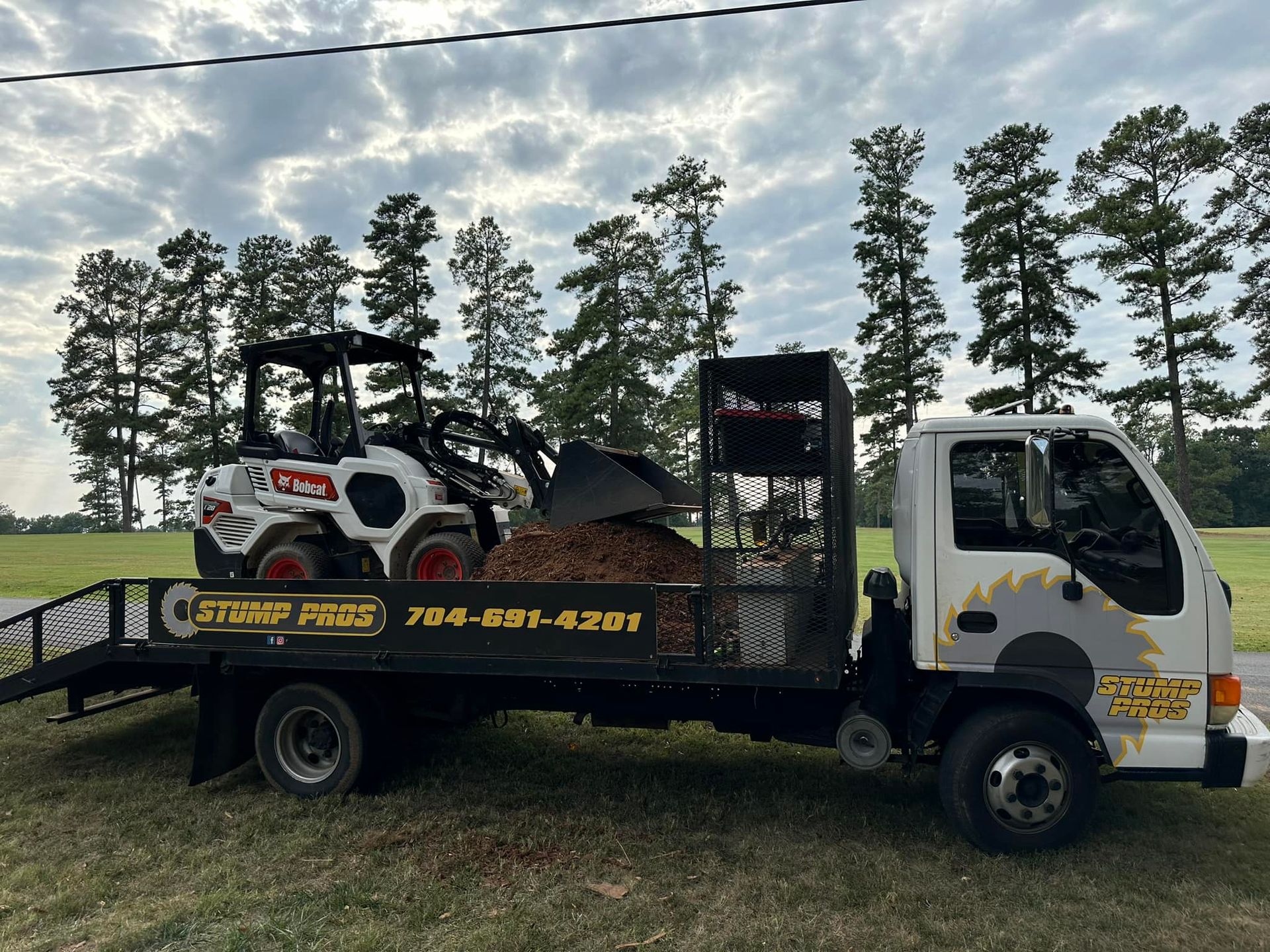 A tow truck with a bulldozer on the back is parked in a field.