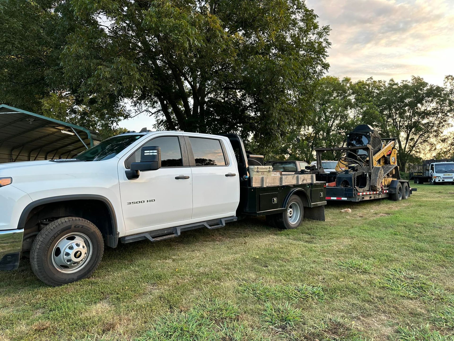 A white truck is towing a forklift in a field.