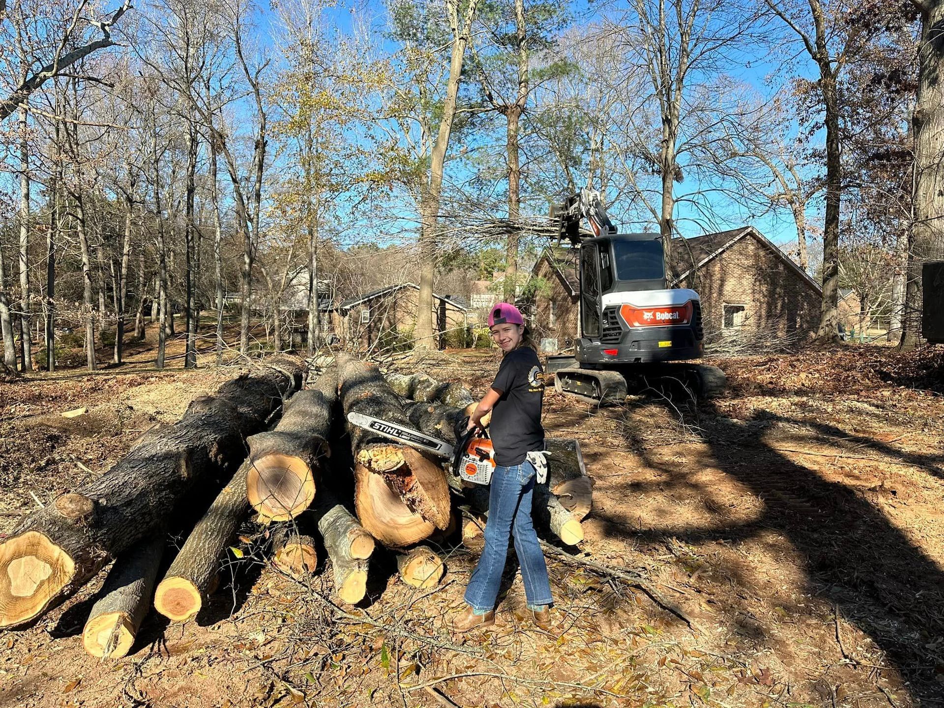 A man is cutting a tree with a chainsaw in front of a pile of logs.