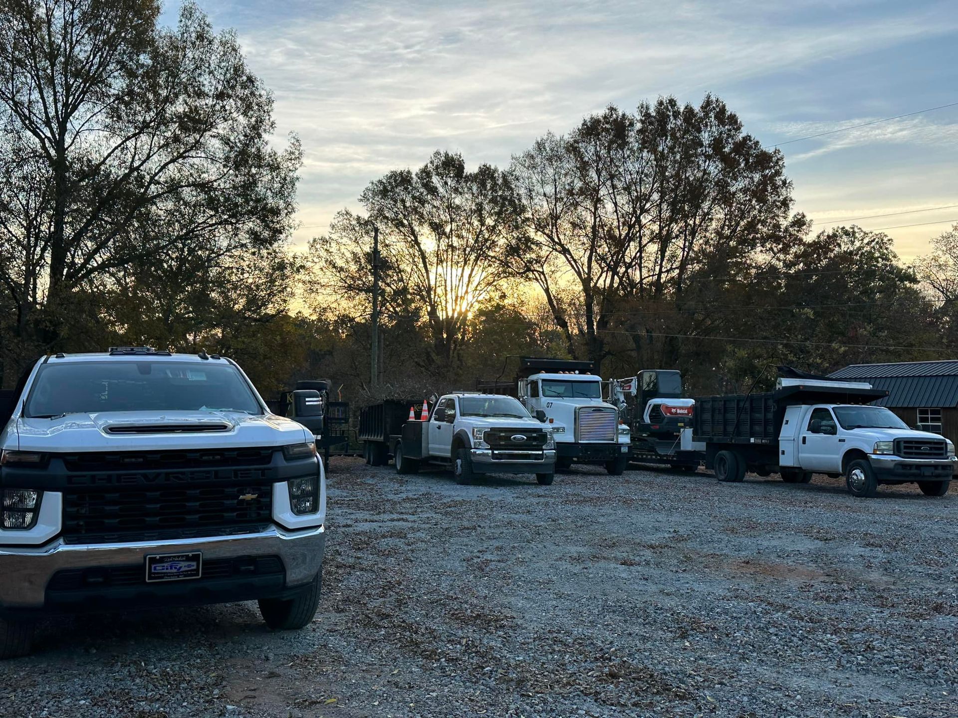 A row of trucks are parked in a gravel lot.