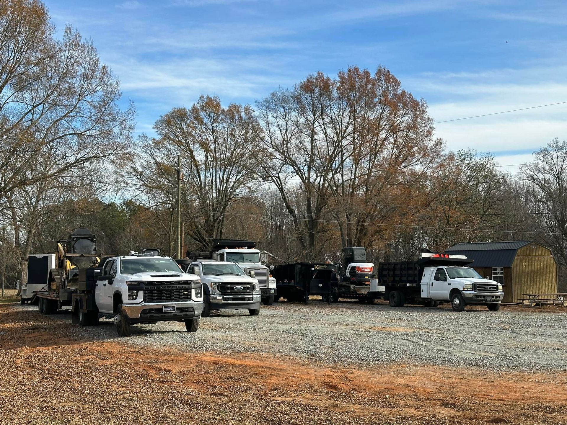 A row of trucks are parked in a gravel lot.