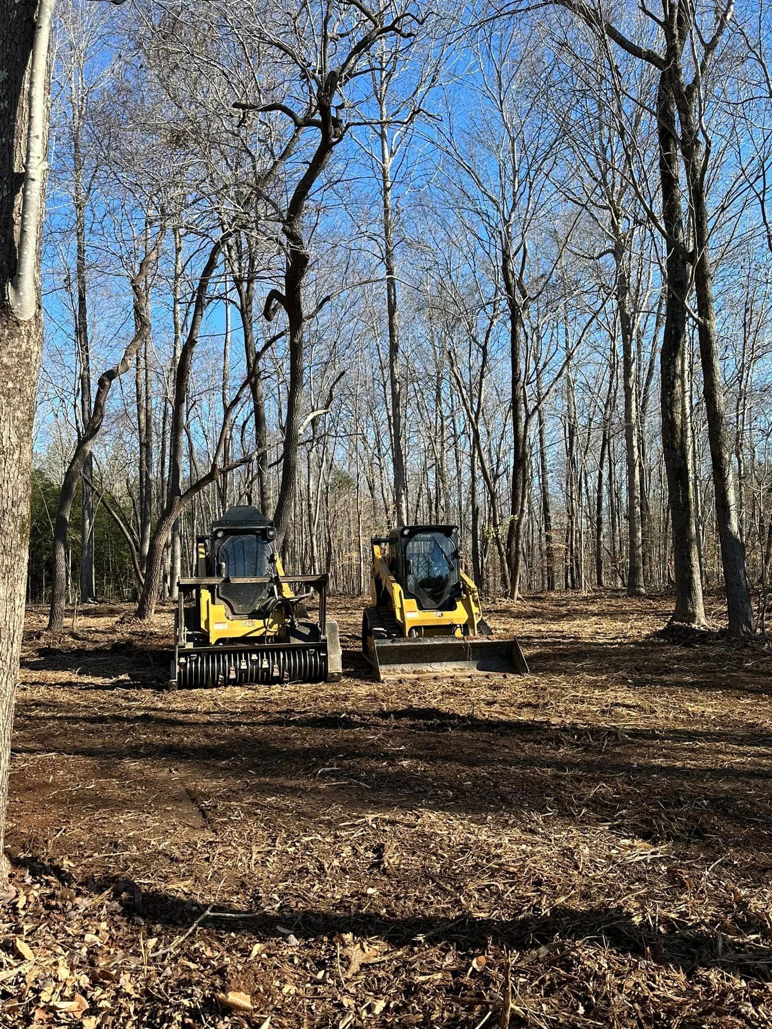Two bulldozers are parked in the middle of a forest.