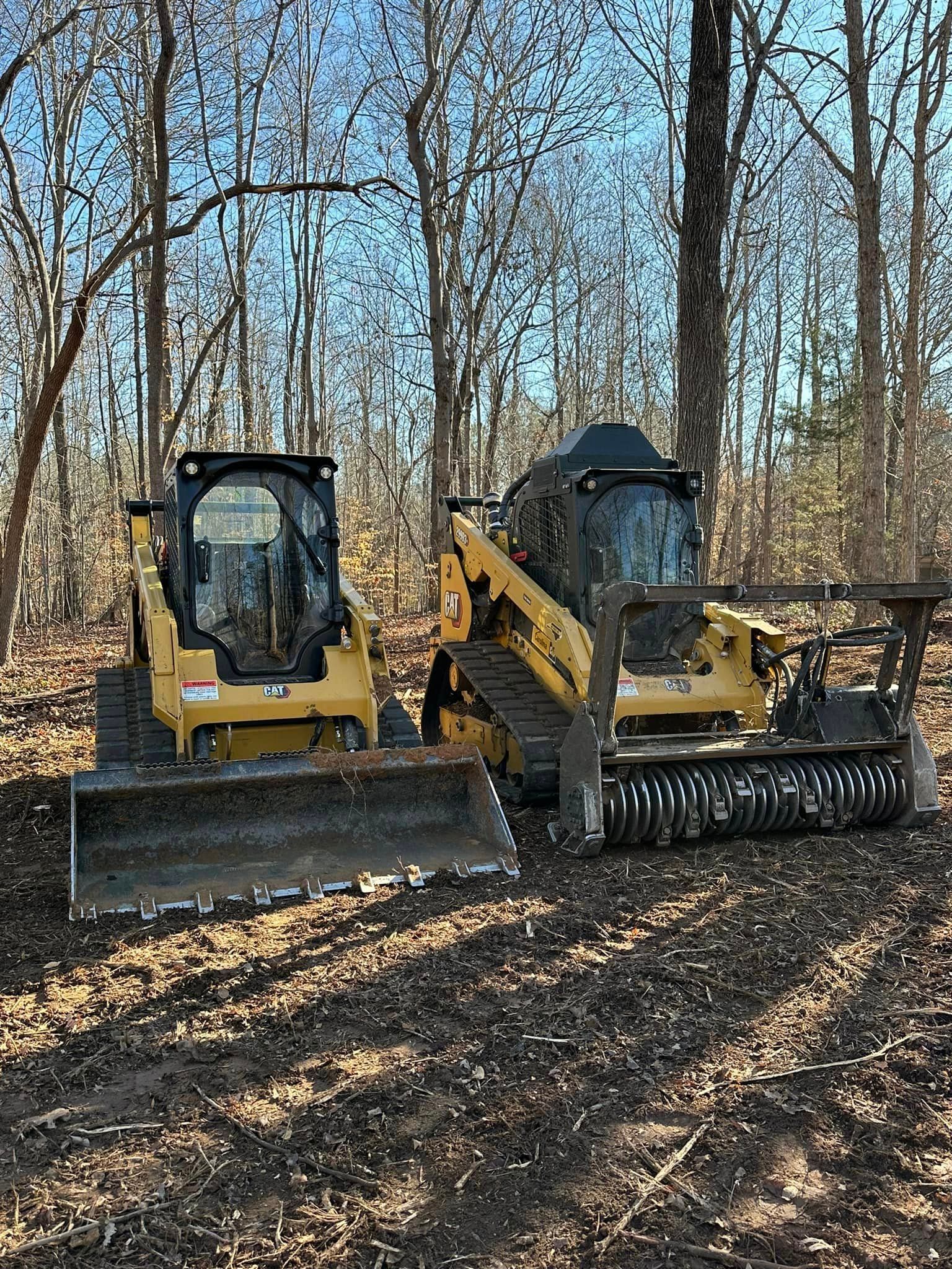 Two bulldozers are parked next to each other in the woods.