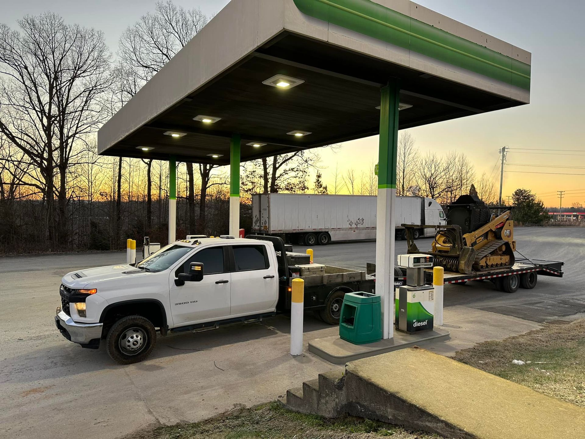 A white truck is parked under a canopy at a gas station.