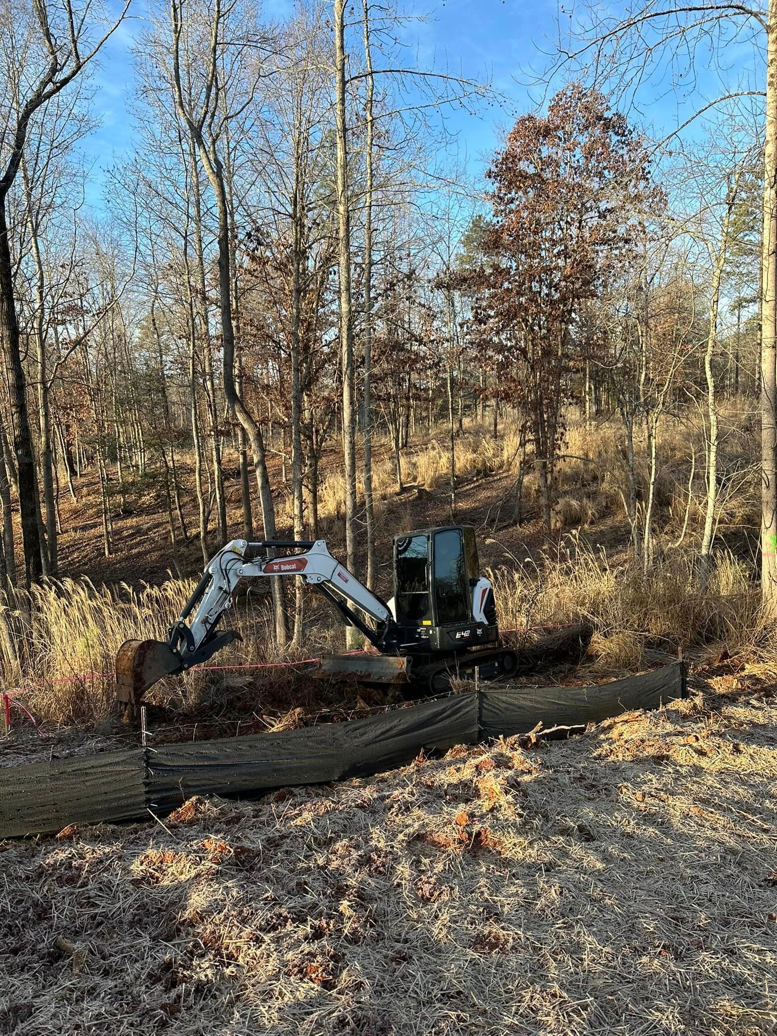 A small excavator is sitting in the middle of a forest.