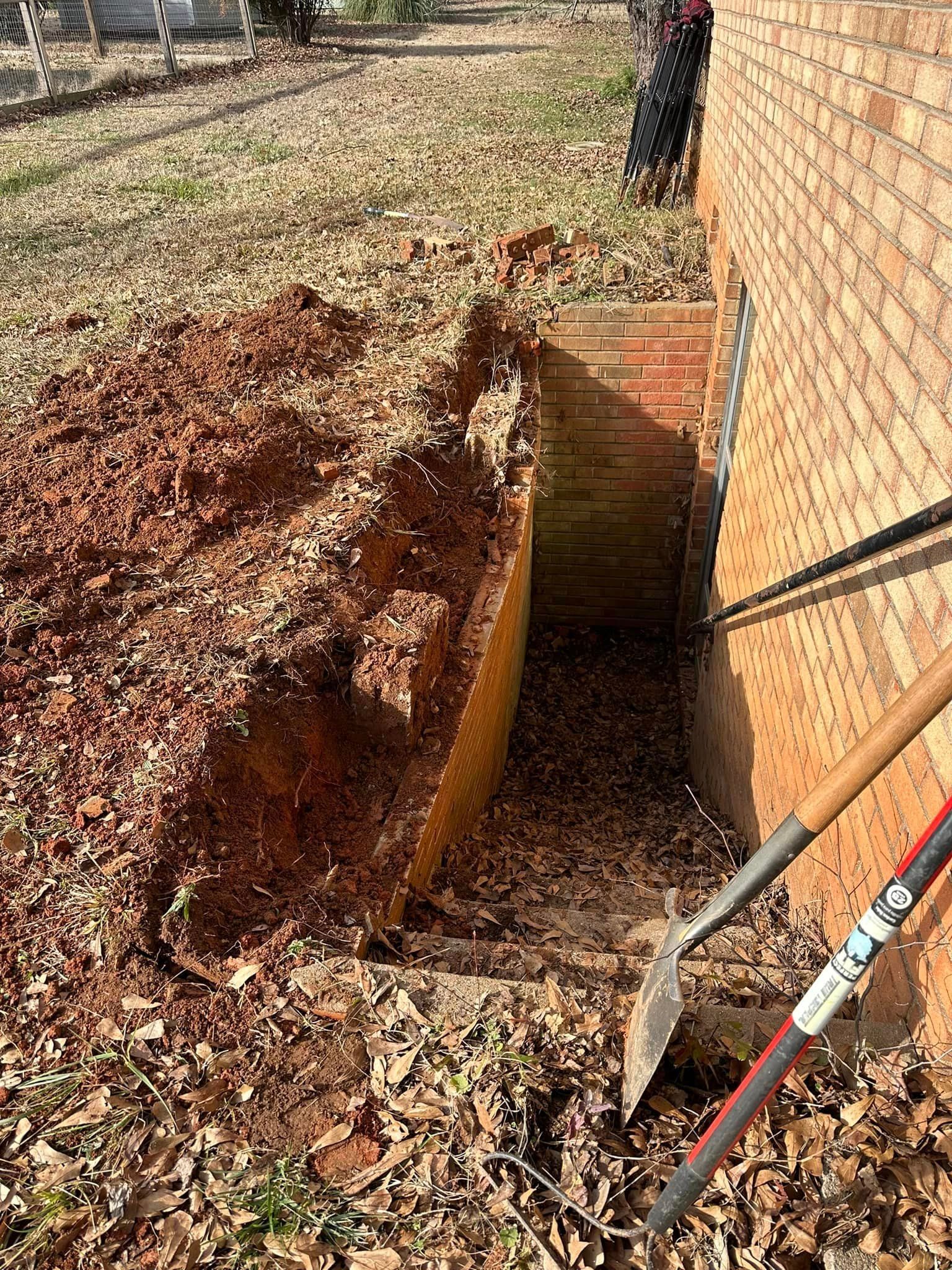 A hole in the ground next to a brick wall with a shovel and rake.