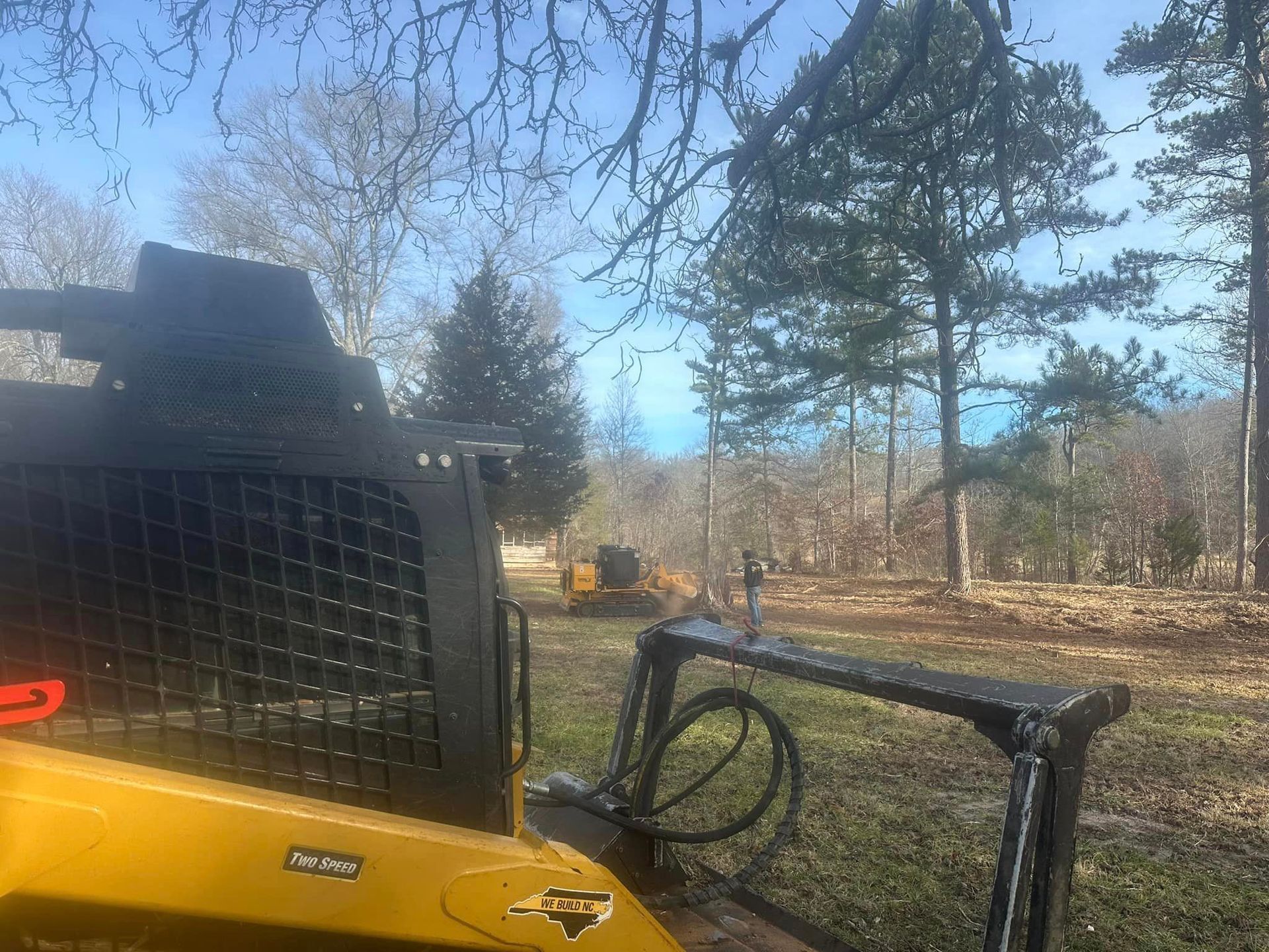 A yellow tractor is parked in a field with trees in the background.