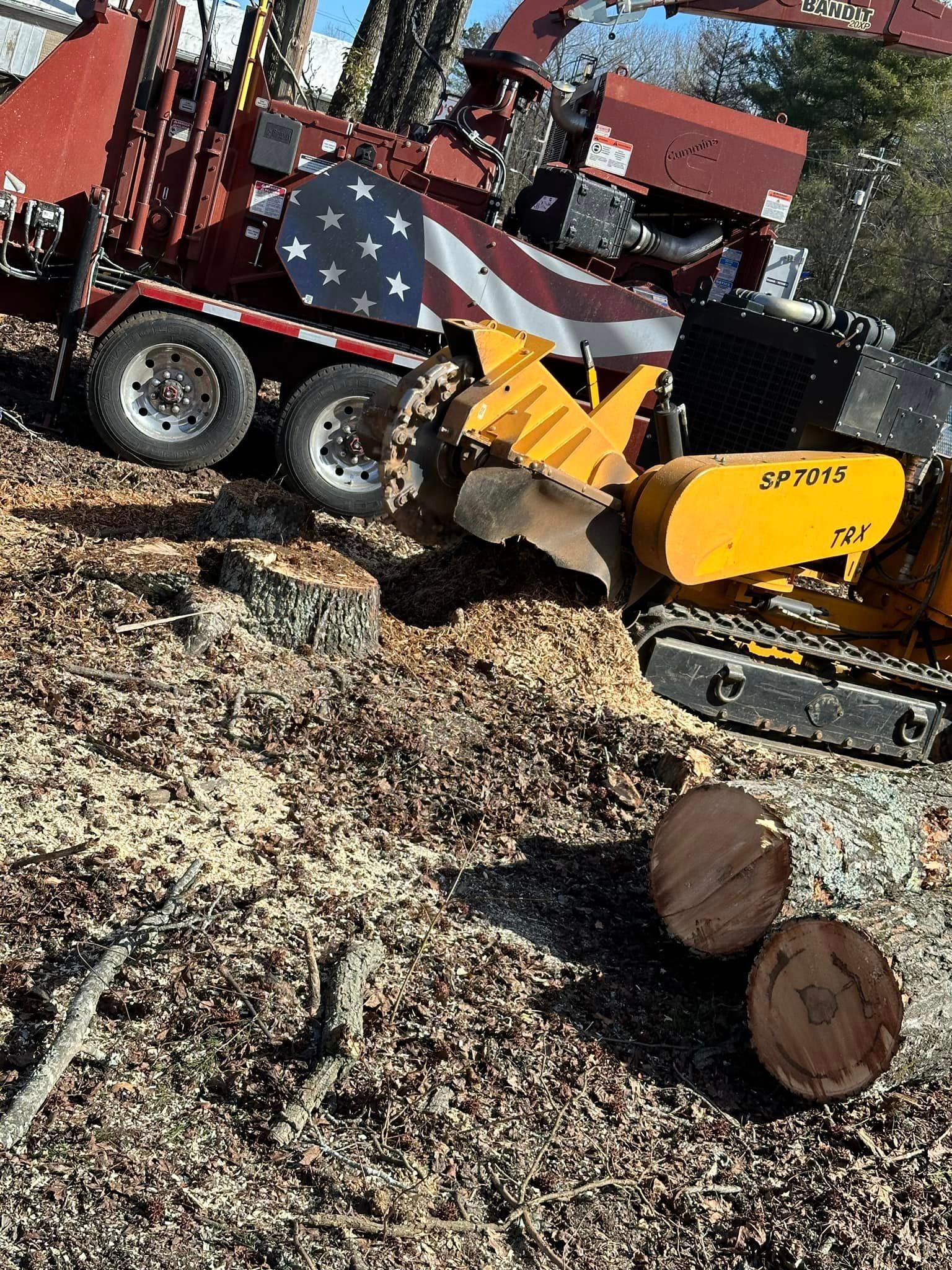 A tree stump grinder with an american flag on the back is cutting a tree stump.