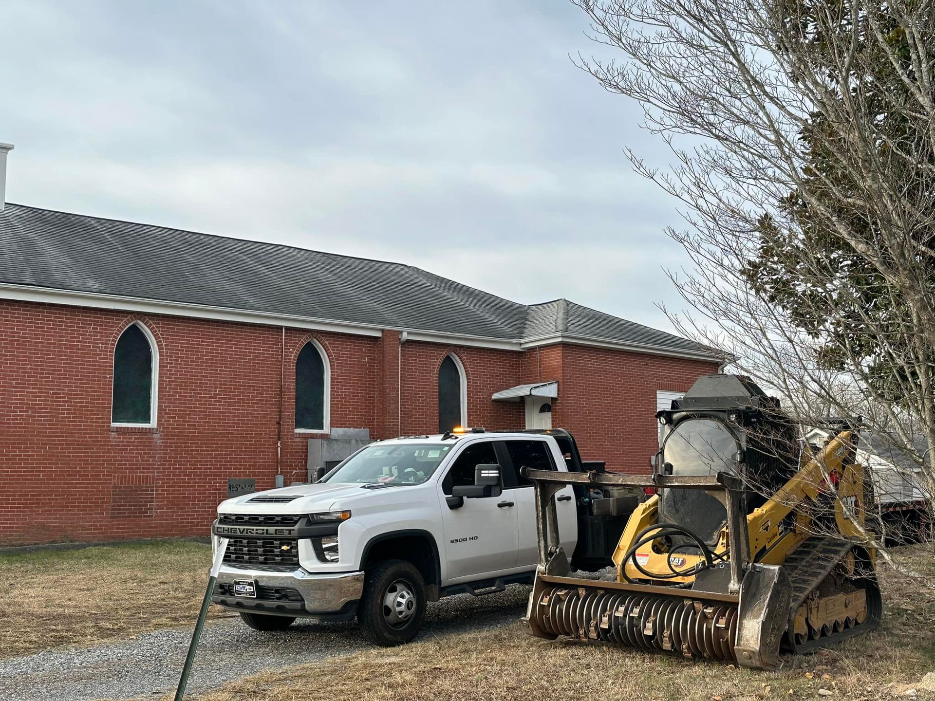A white truck and a yellow bulldozer are parked in front of a brick building.