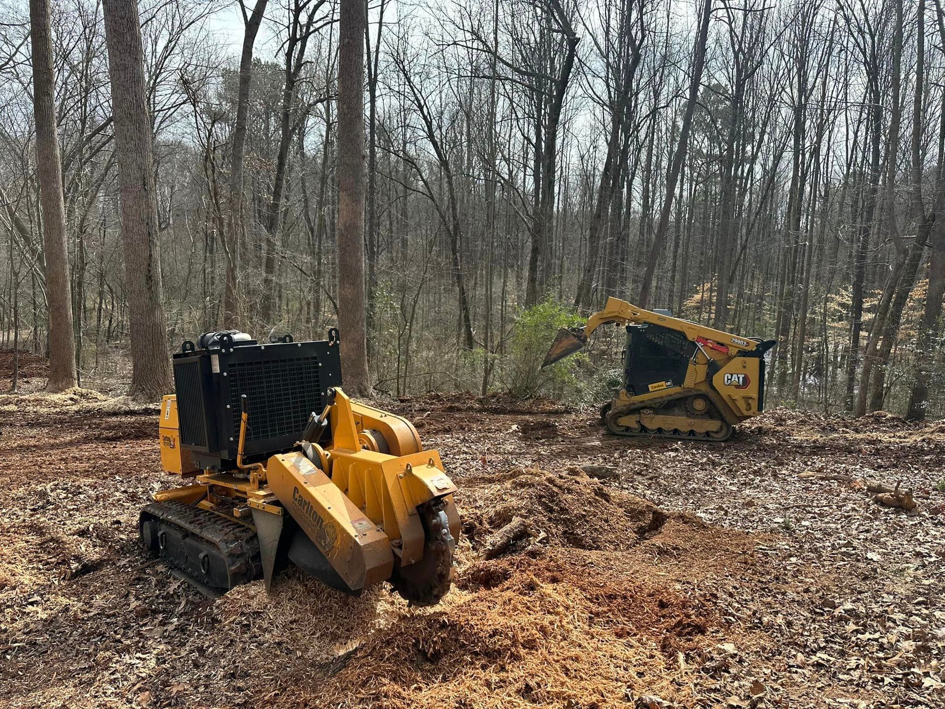 A stump grinder is sitting in the middle of a forest next to a bulldozer.