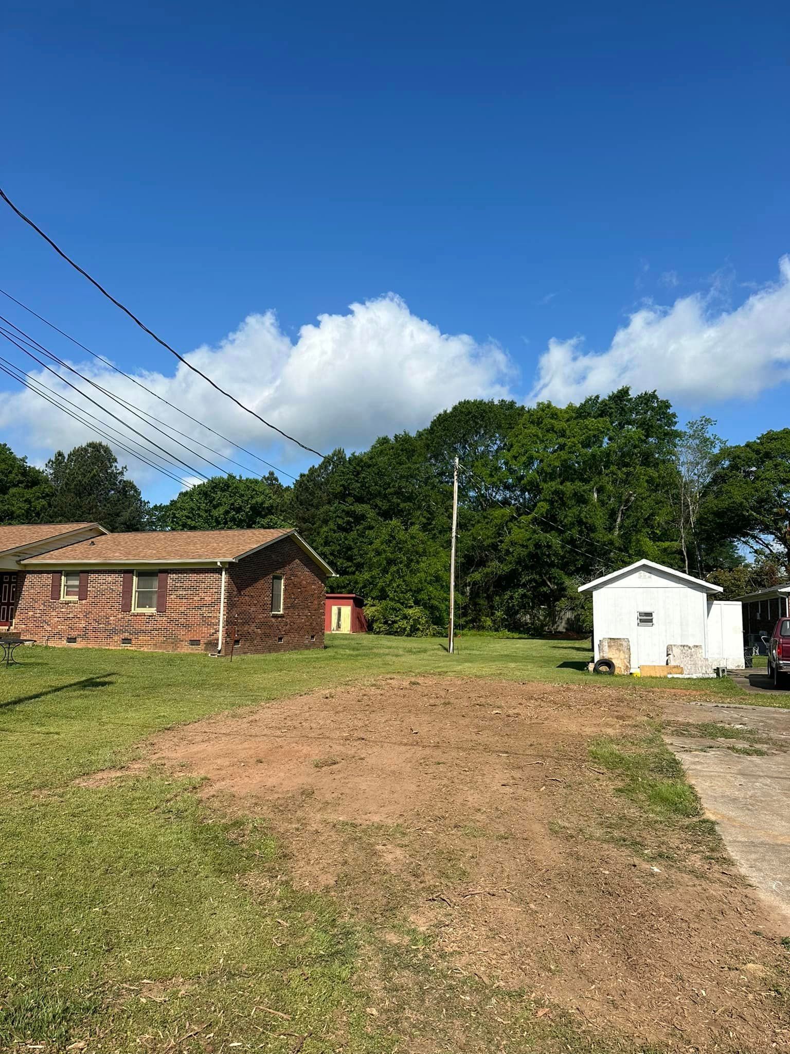 A house is sitting in the middle of a grassy field next to a shed.
