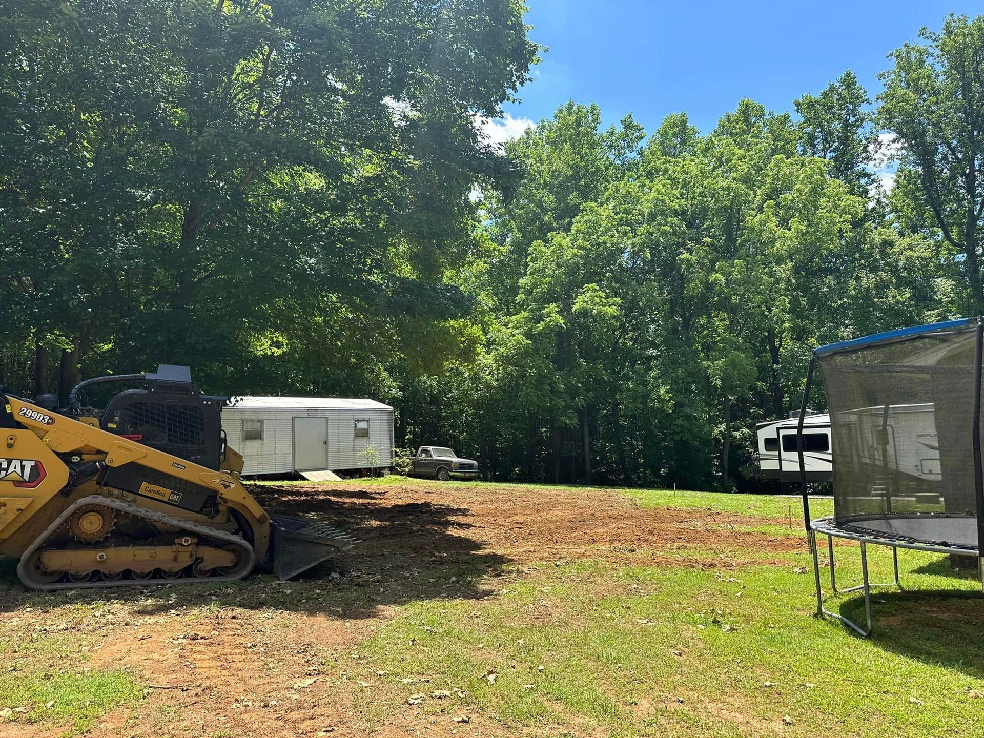 A bulldozer is sitting in the middle of a grassy field next to a trampoline.