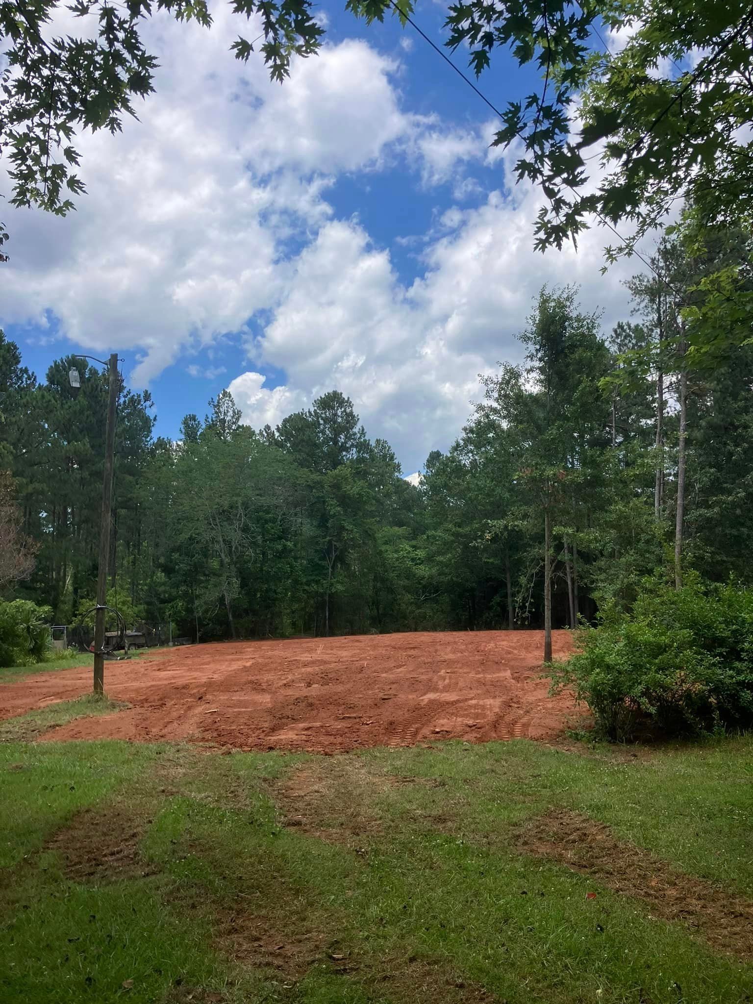 A dirt field with trees in the background and a blue sky with clouds