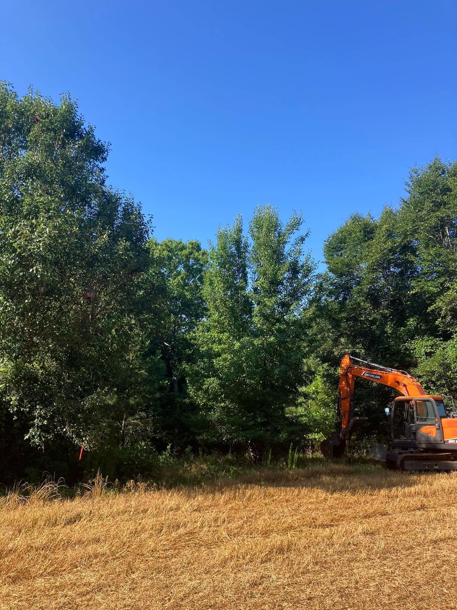 A large orange excavator is sitting in a field with trees in the background.