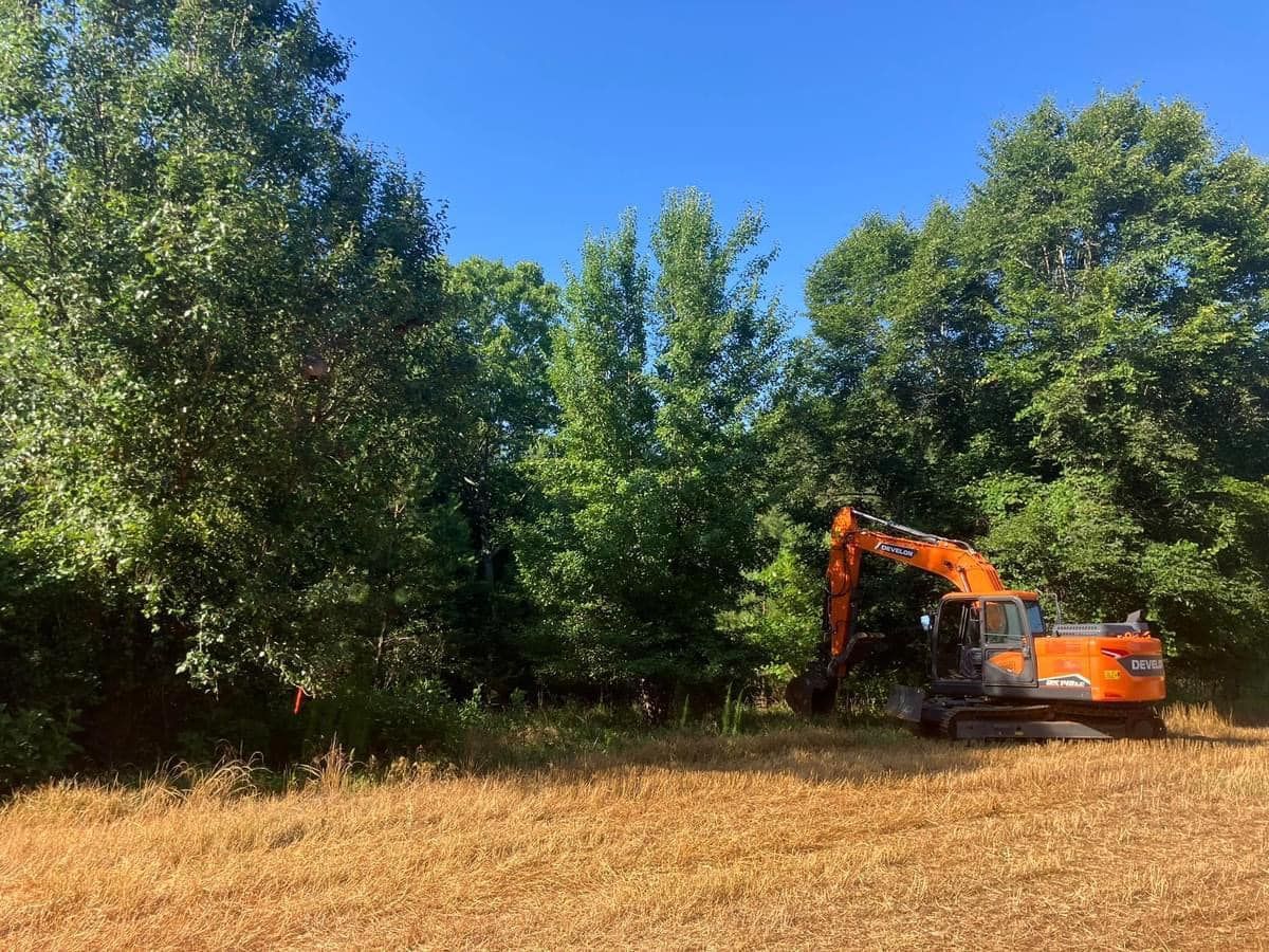 A large orange excavator is sitting in the middle of a field surrounded by trees.
