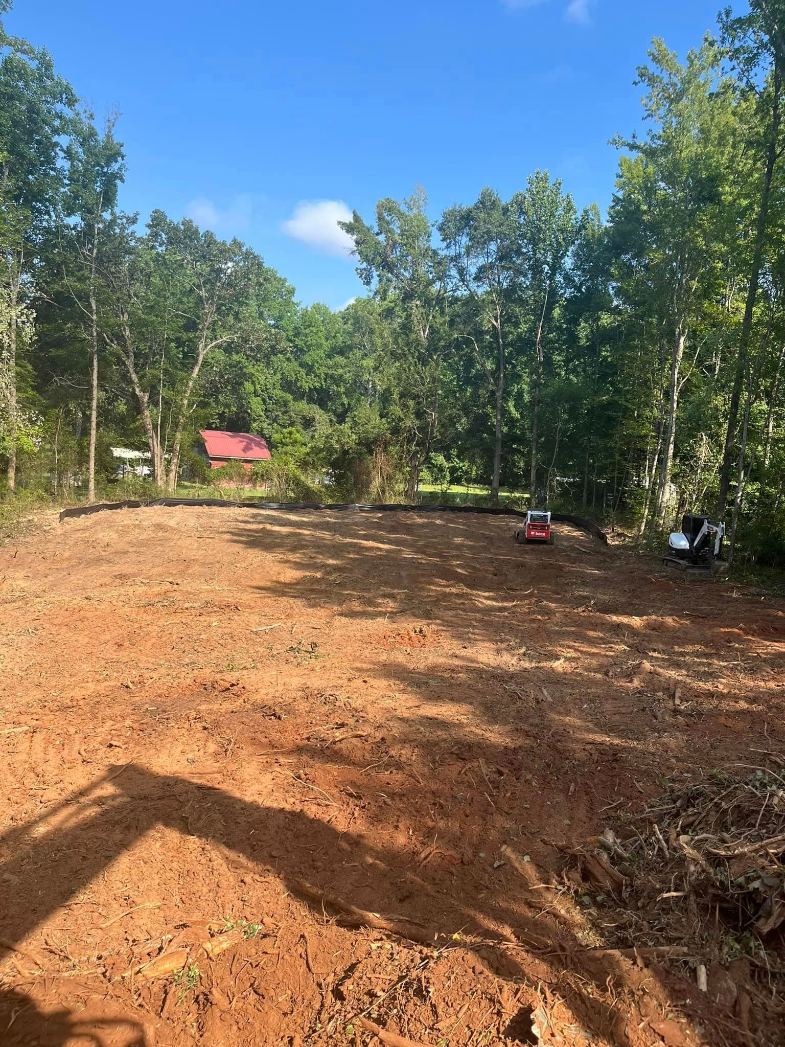 A large dirt field with trees in the background and a house in the background.