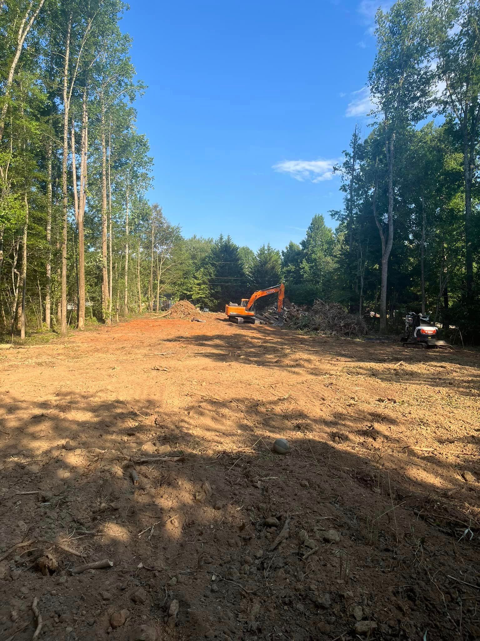 A large dirt field with trees in the background and a bulldozer in the middle.