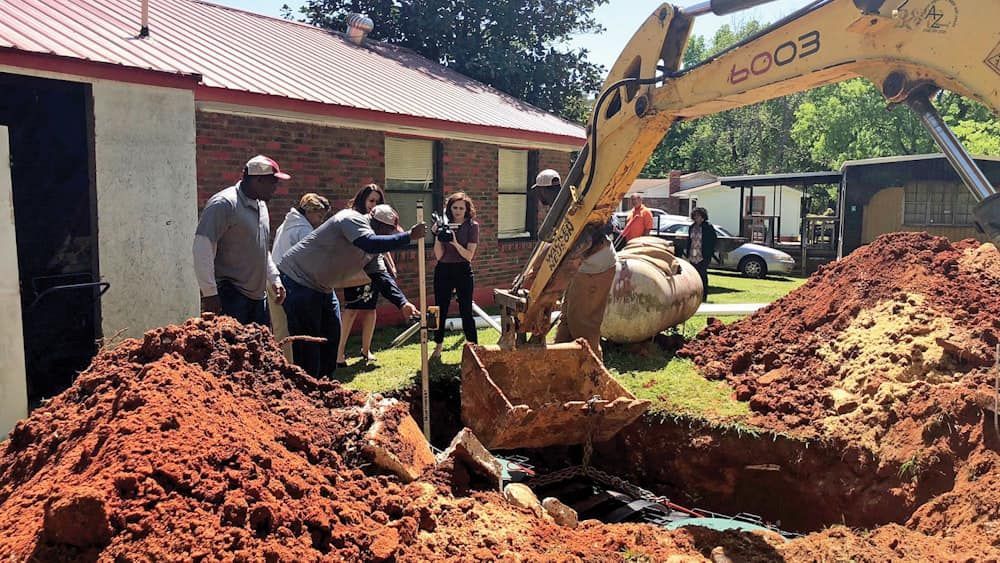 A yellow excavator is digging a hole in the ground in front of a house.