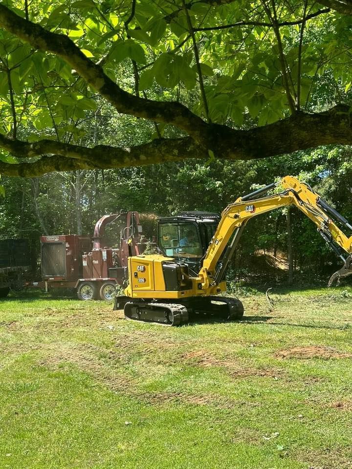A yellow excavator is sitting on top of a lush green field.